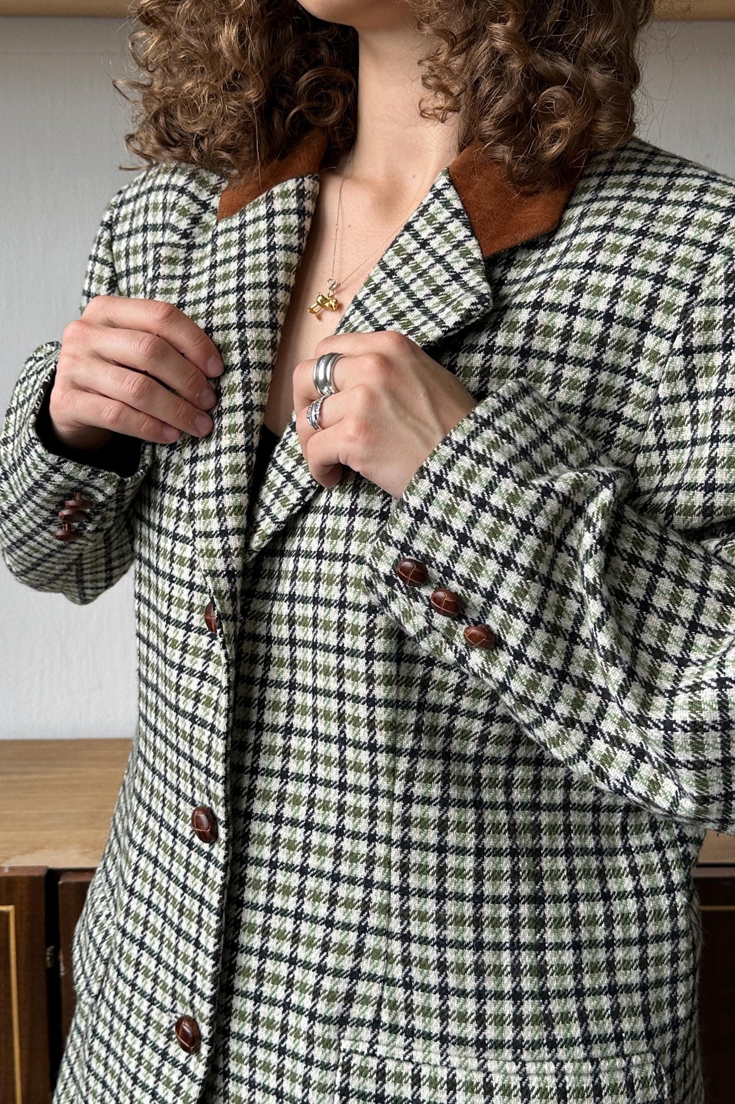 A person wearing a black and white checkered jacket with brown collar buttons, adjusting the collar.