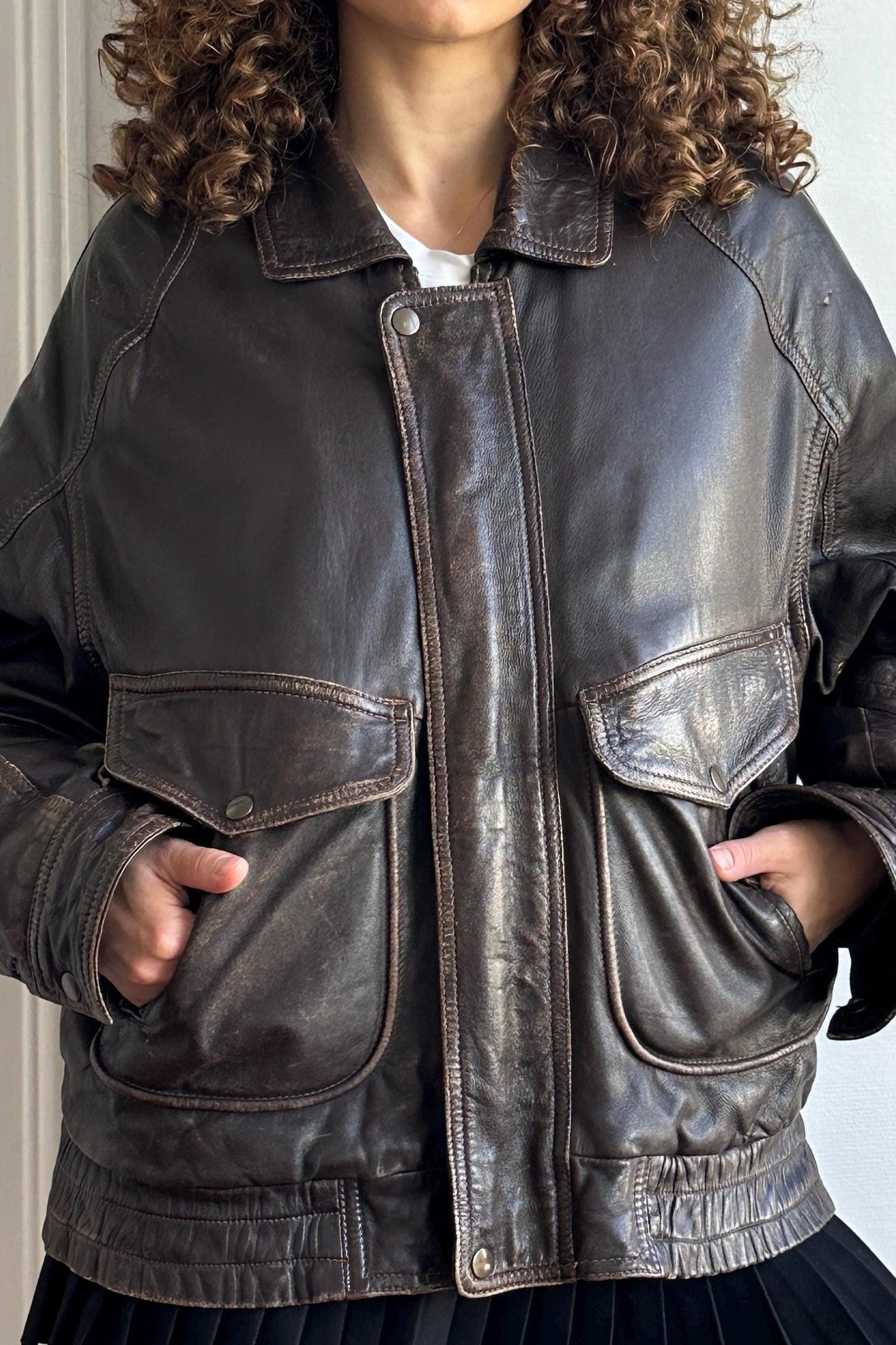 A close-up of a person wearing a brown leather jacket with a collar and two pockets.