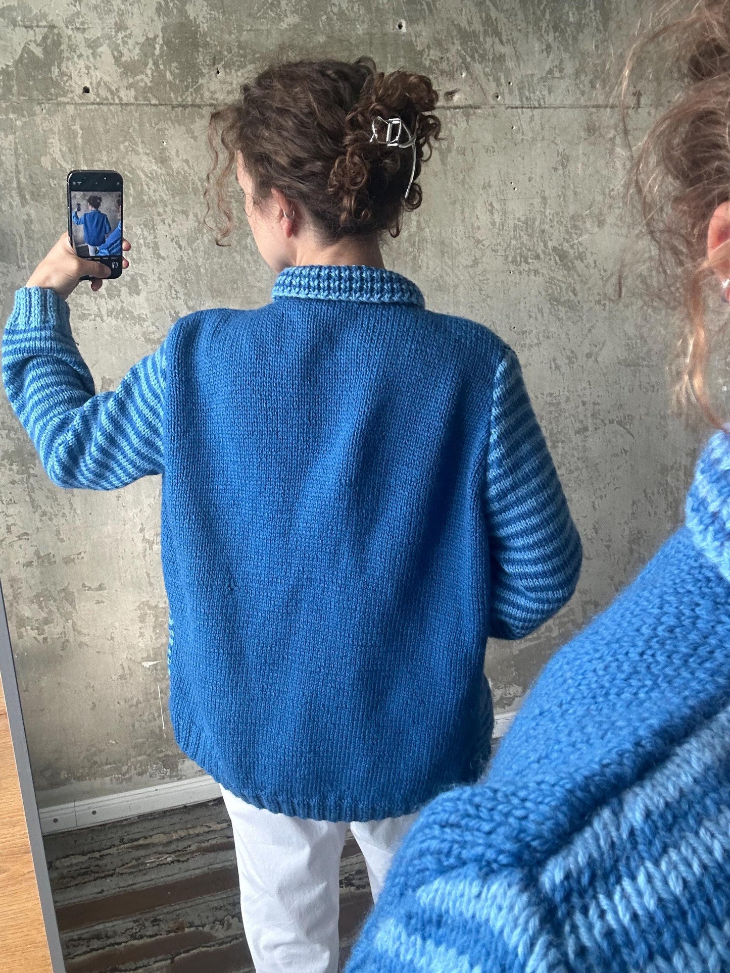 A person is taking a selfie with a smartphone, wearing a blue and white striped sweater.