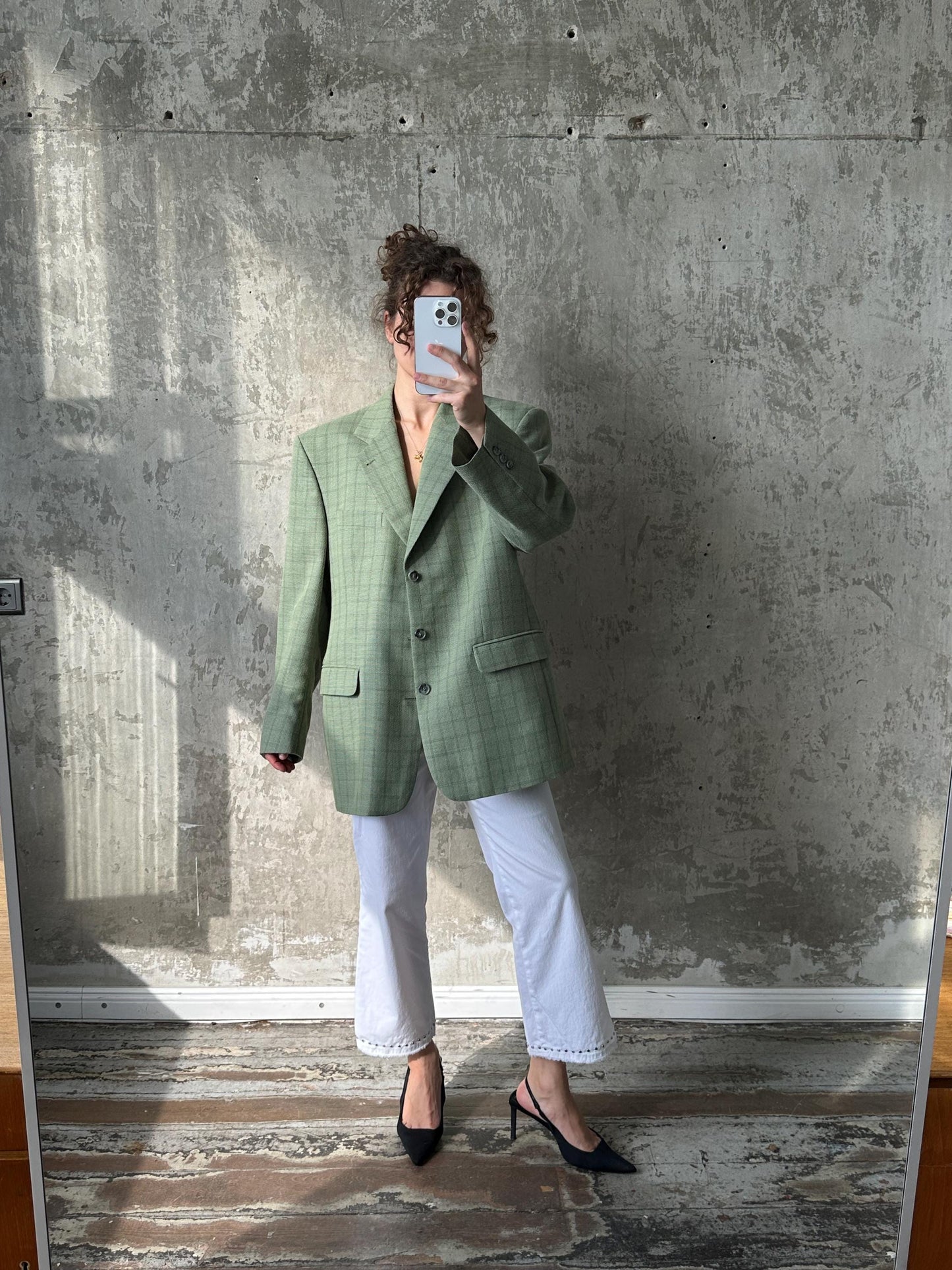 A person is taking a selfie in front of a concrete wall, holding a phone up to their face.