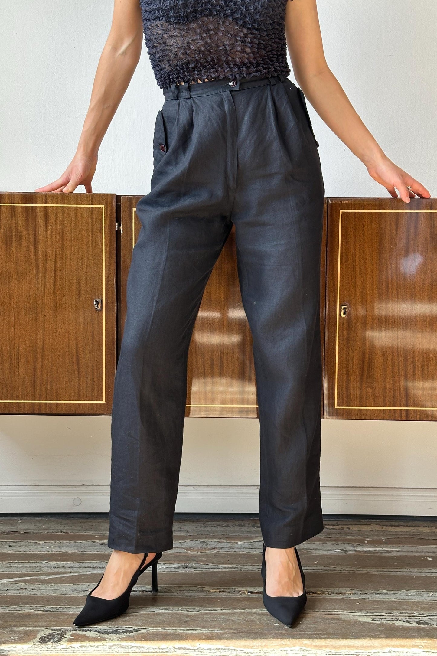 A person wearing a black top and gray pants stands in front of a wooden cabinet.