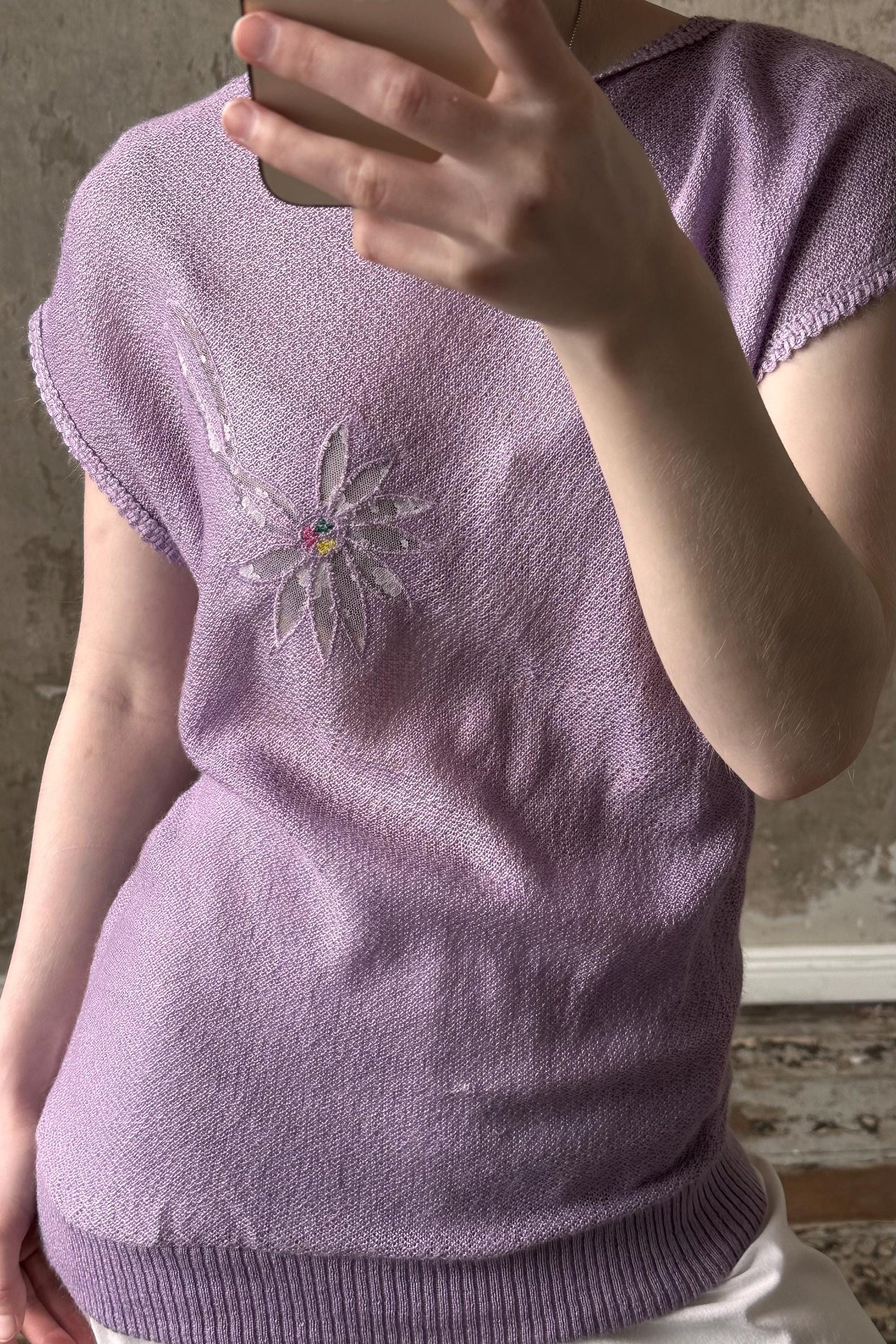 A person is taking a selfie with a purple sweater featuring a flower design on the front.