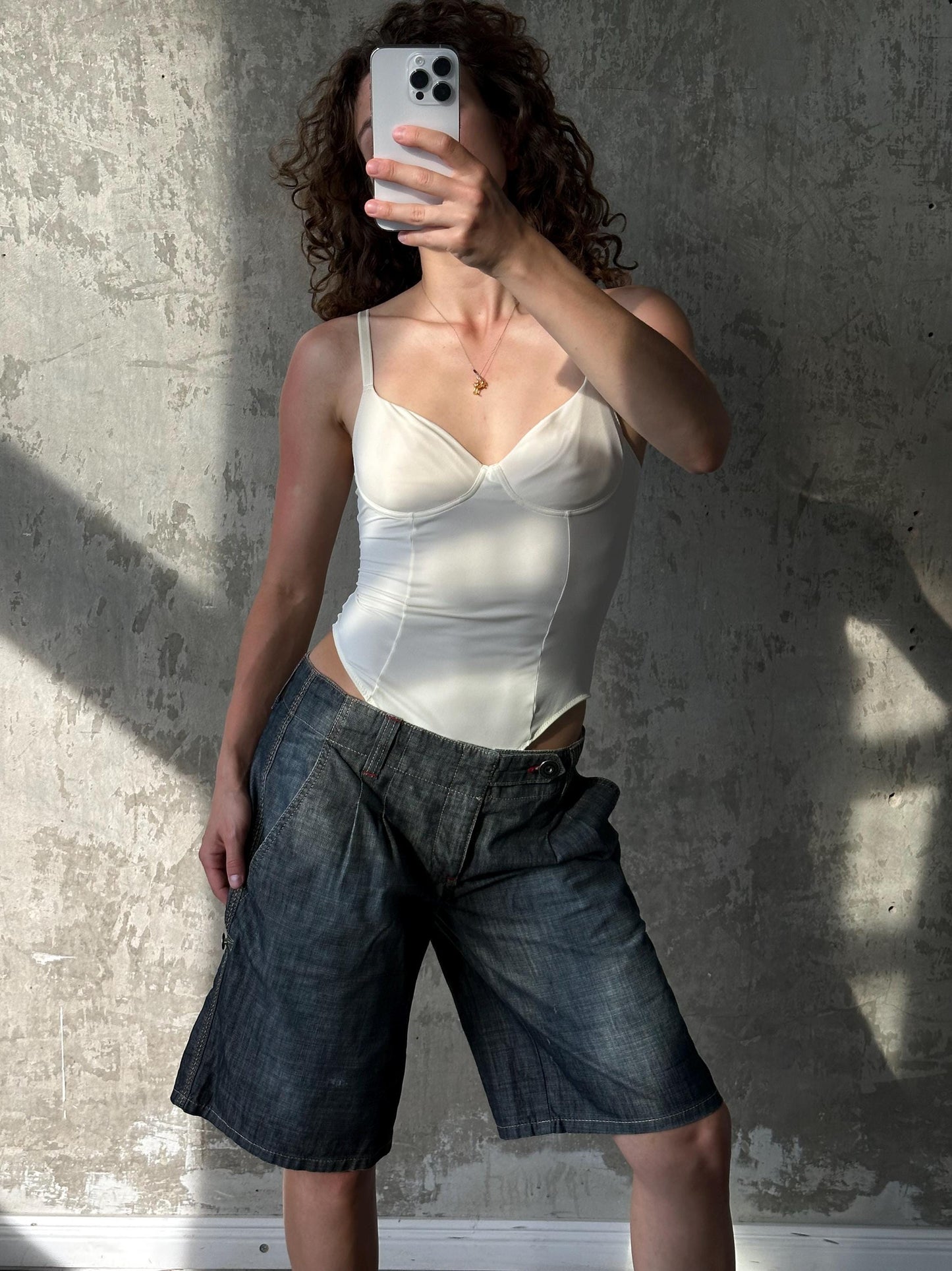 A woman is taking a selfie with her phone, holding it up to her face against a concrete wall.