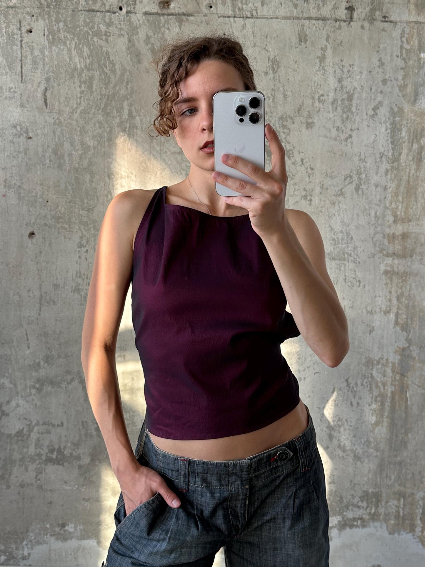 A woman is taking a selfie with her iPhone, holding the device up to her face against a concrete wall.