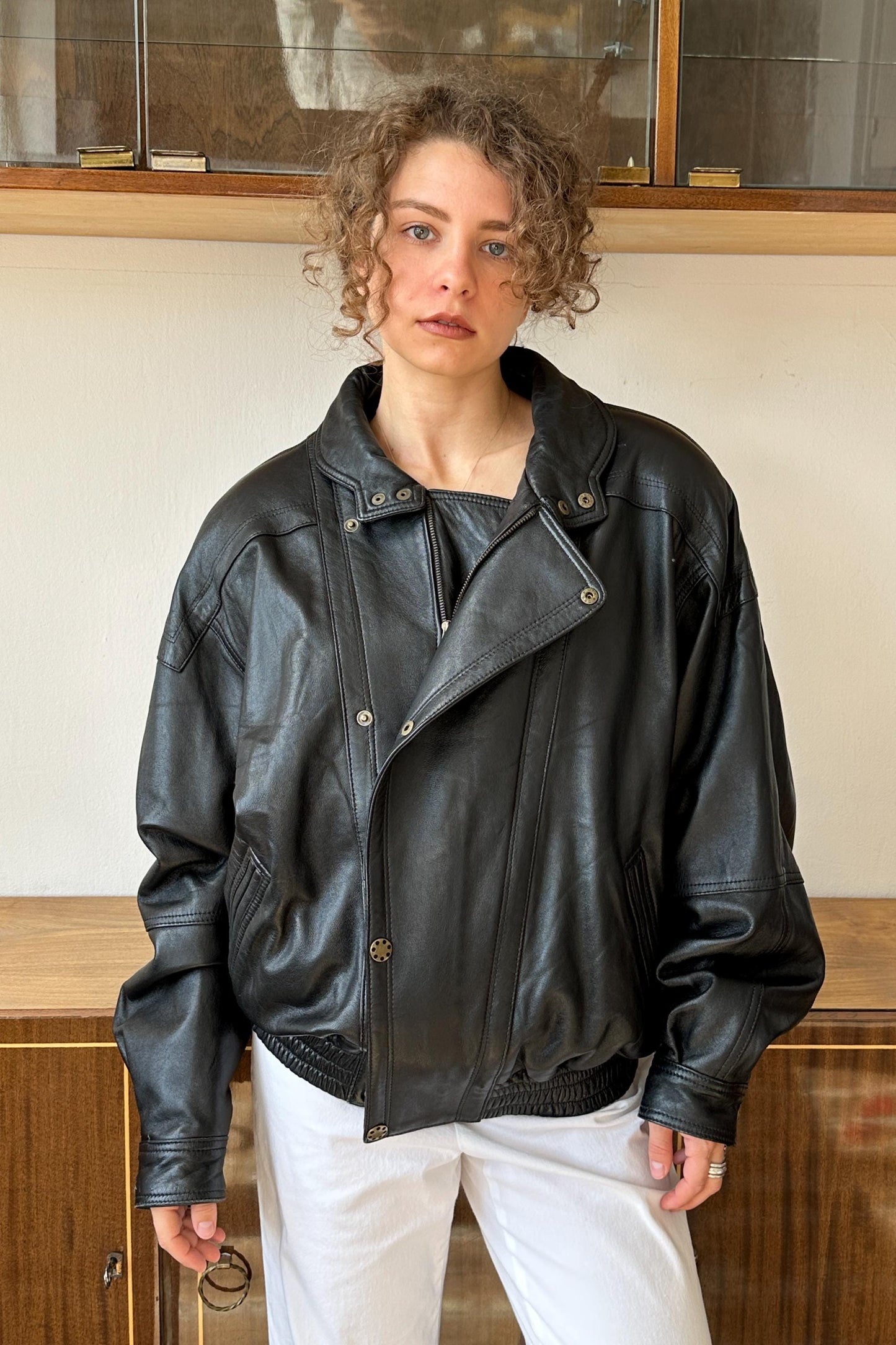 A woman wearing a black leather jacket stands in front of a glass display case.