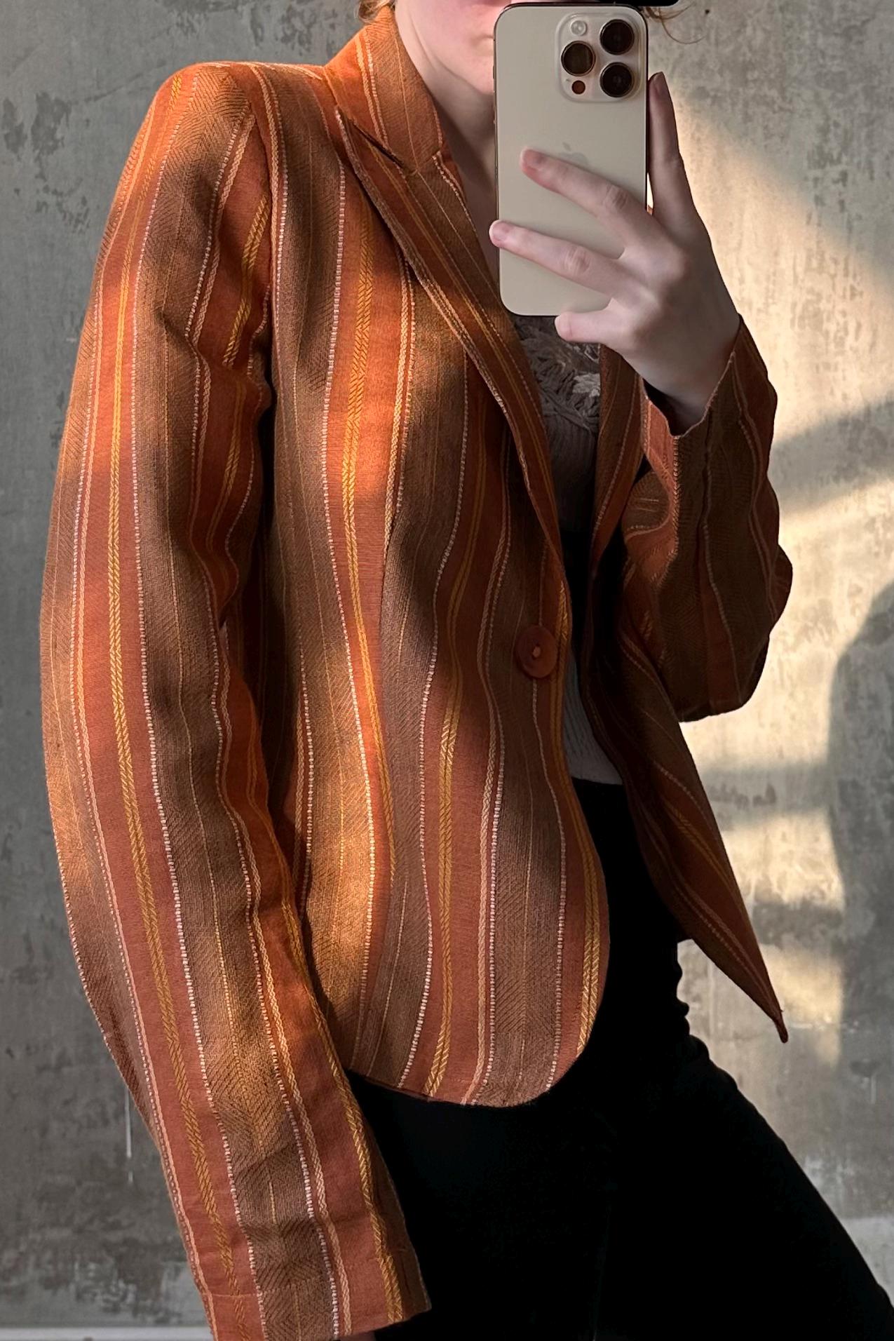 A person is taking a selfie with a striped orange and brown jacket, holding a smartphone in their hand.