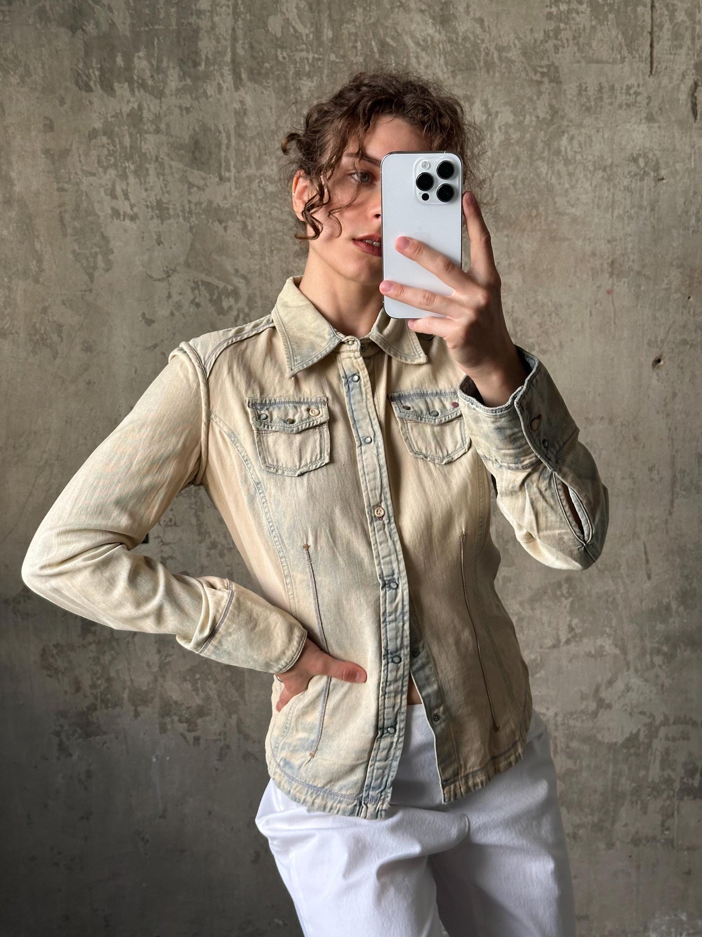 A woman is taking a selfie with her iPhone, holding the device up to her face against a concrete wall background.