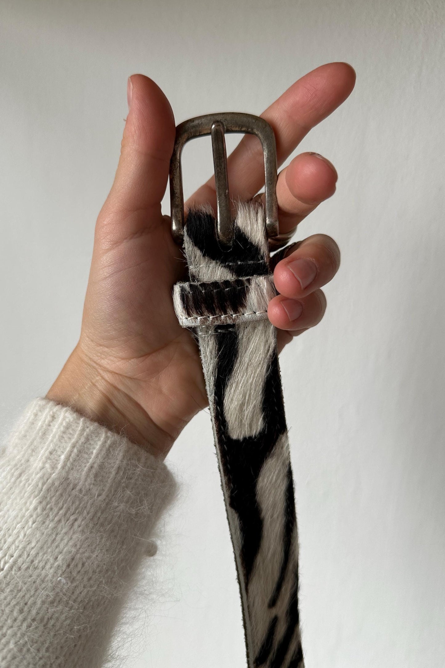 A hand holding a black and white zebra print belt against a white background.
