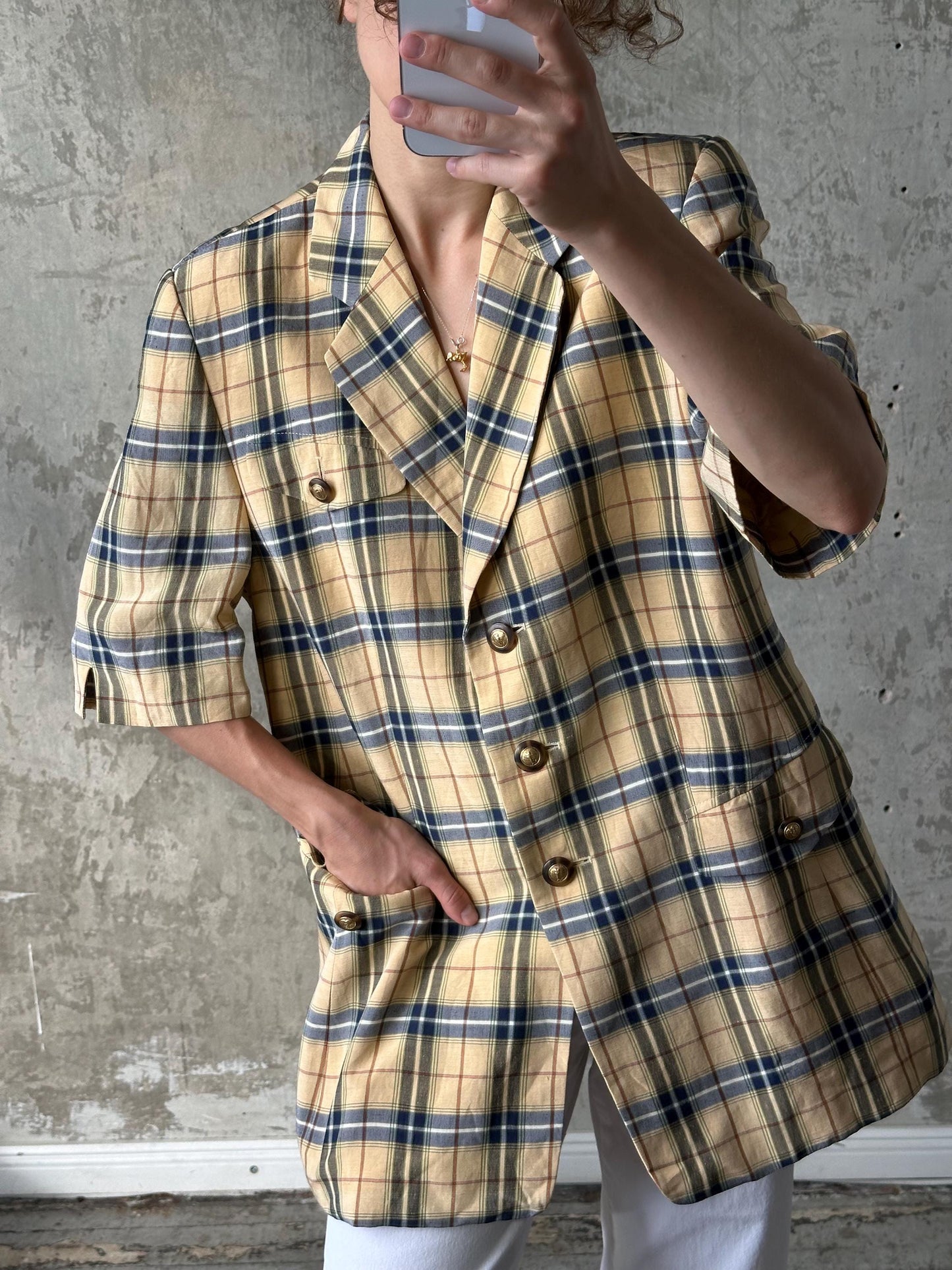 A person is taking a selfie with a plaid jacket on, holding a phone up to their face.