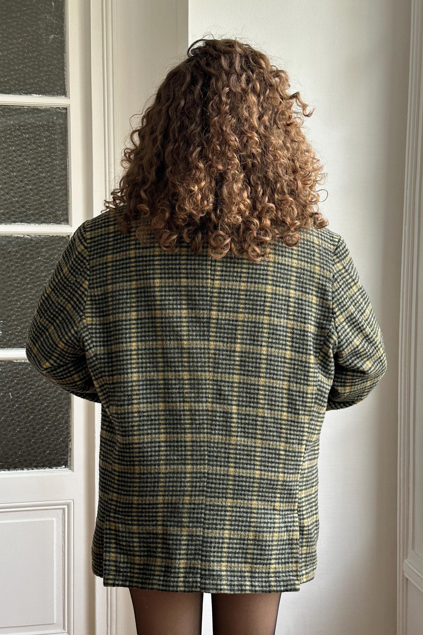 the back of a person wearing a plaid jacket, with their hair styled in curls.