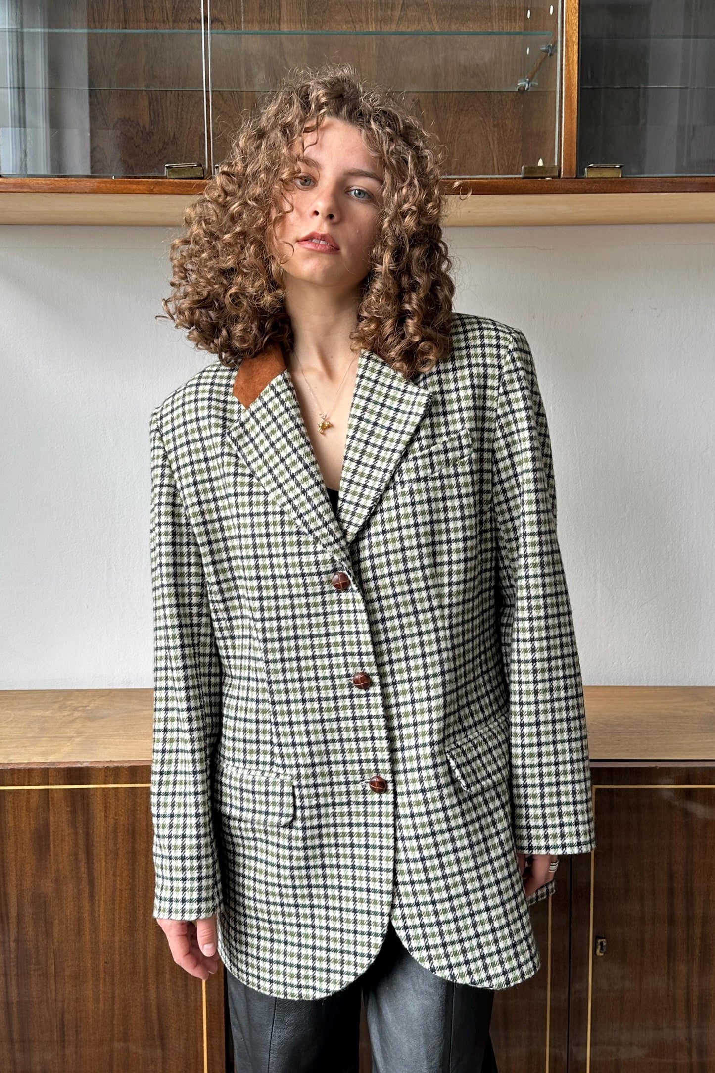 A woman with curly hair wearing a checkered jacket stands in front of a glass display case.