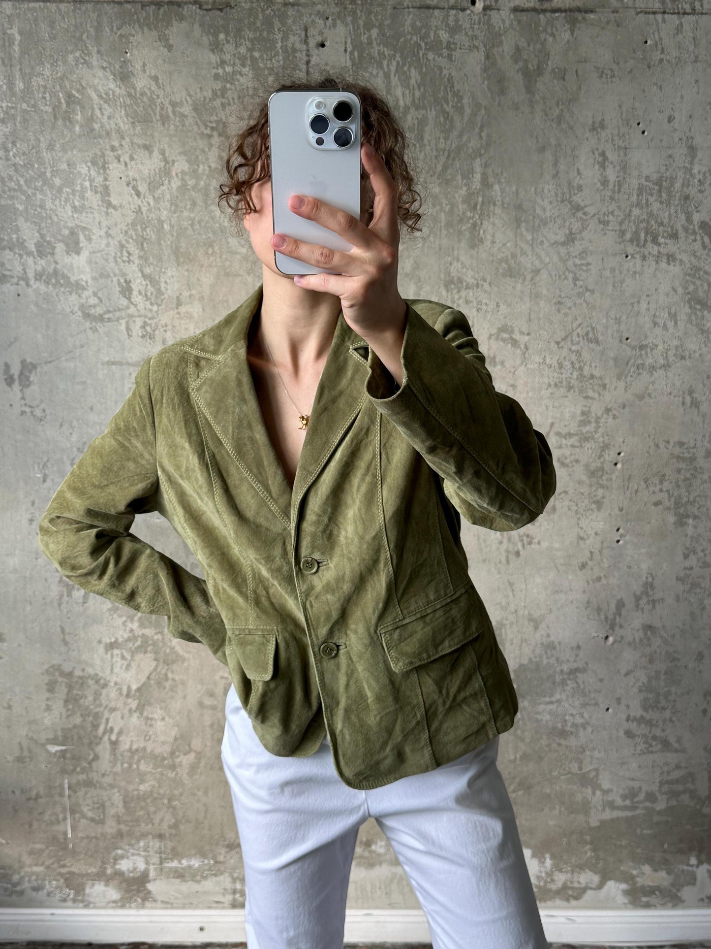 A person is taking a selfie with a smartphone, holding the phone up to their face against a concrete wall background.