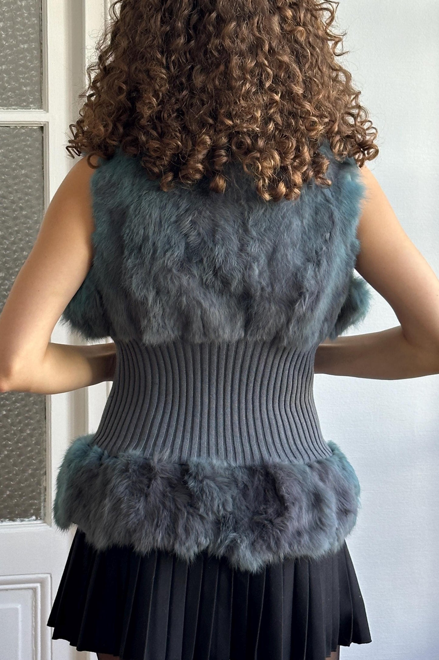 a woman with curly hair wearing a gray sweater vest and a black skirt.