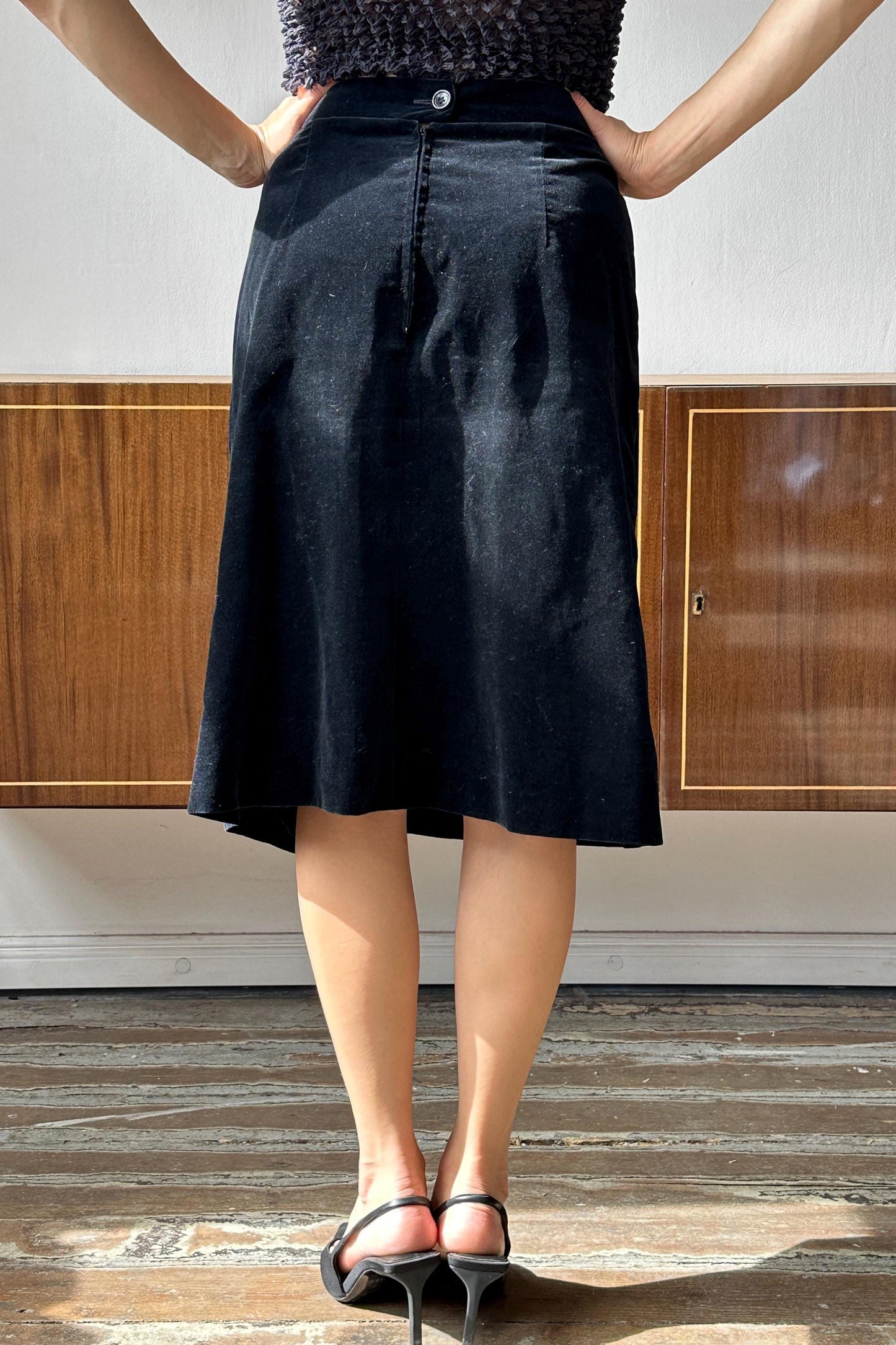 A person wearing a black skirt stands with their hands on their hips, facing away from the camera.