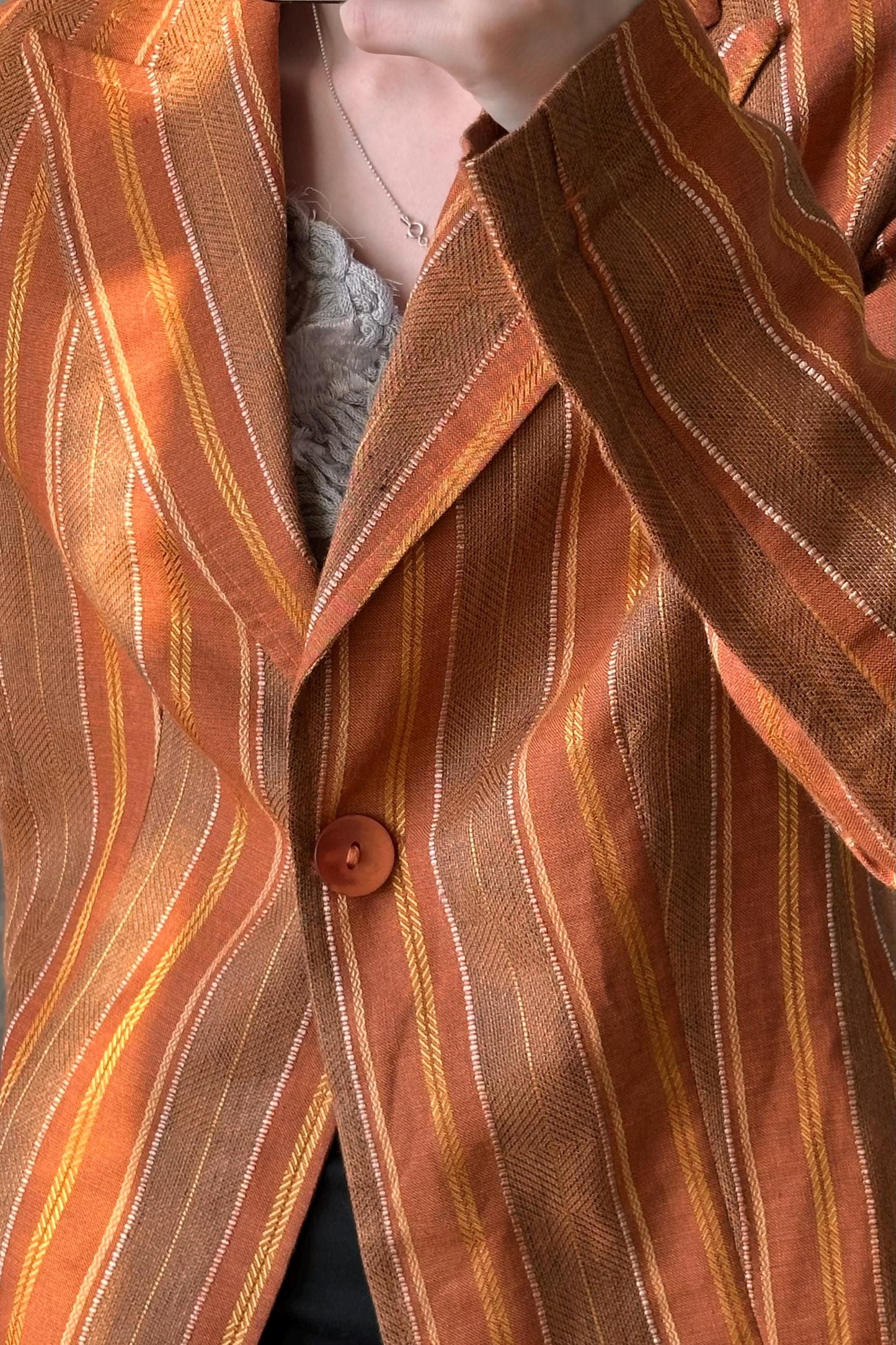 A close-up view of a person wearing a striped orange and brown jacket with a button.