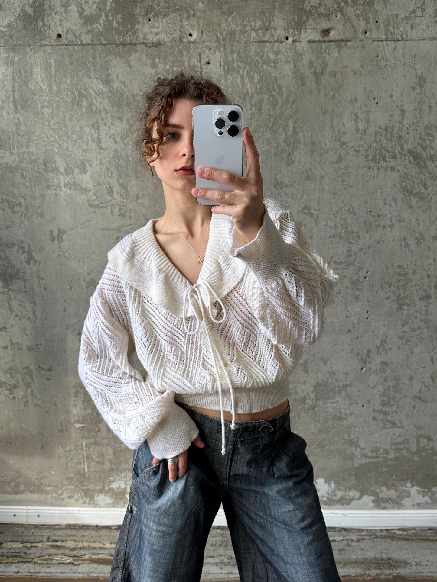 A person is taking a selfie with a smartphone, holding the device up to their face against a concrete wall background.