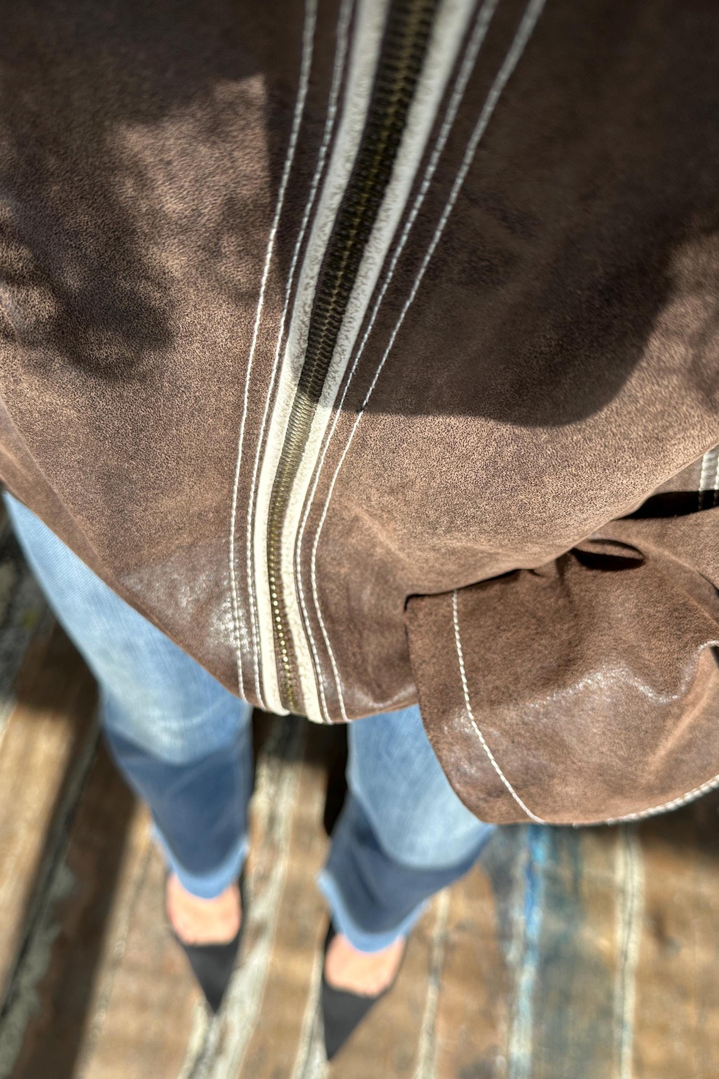 A close-up view of a person's torso and legs wearing a brown jacket with a white zipper stripe.