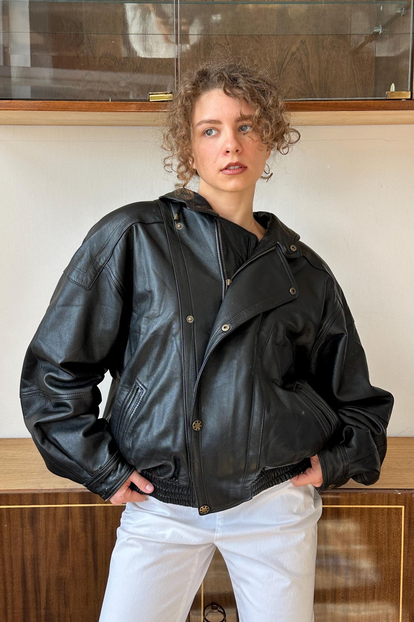 A woman wearing a black leather jacket stands in front of a glass display case.