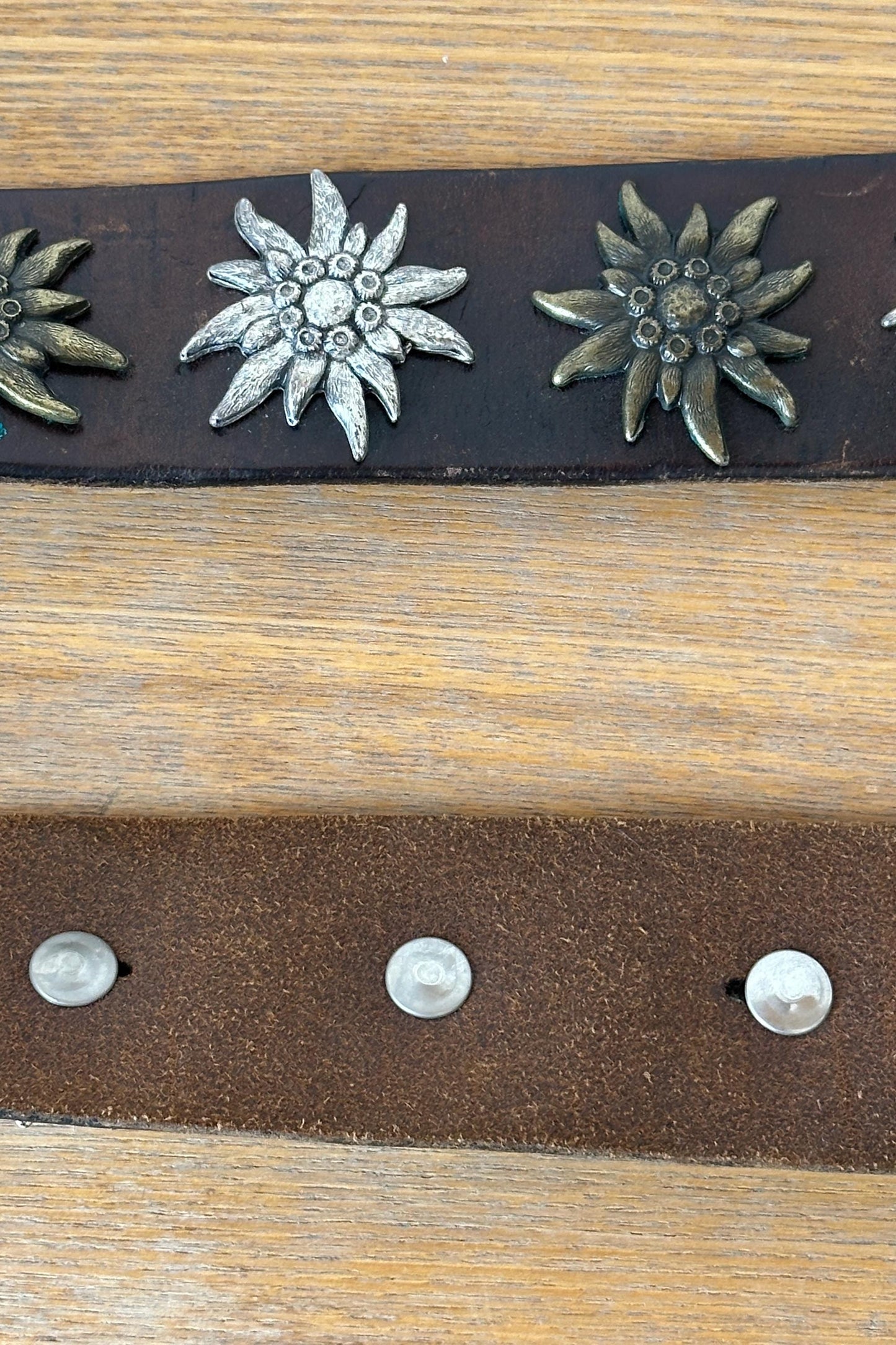 a close-up view of a leather belt with metal decorative elements, including two large metal flowers with pointed petals.