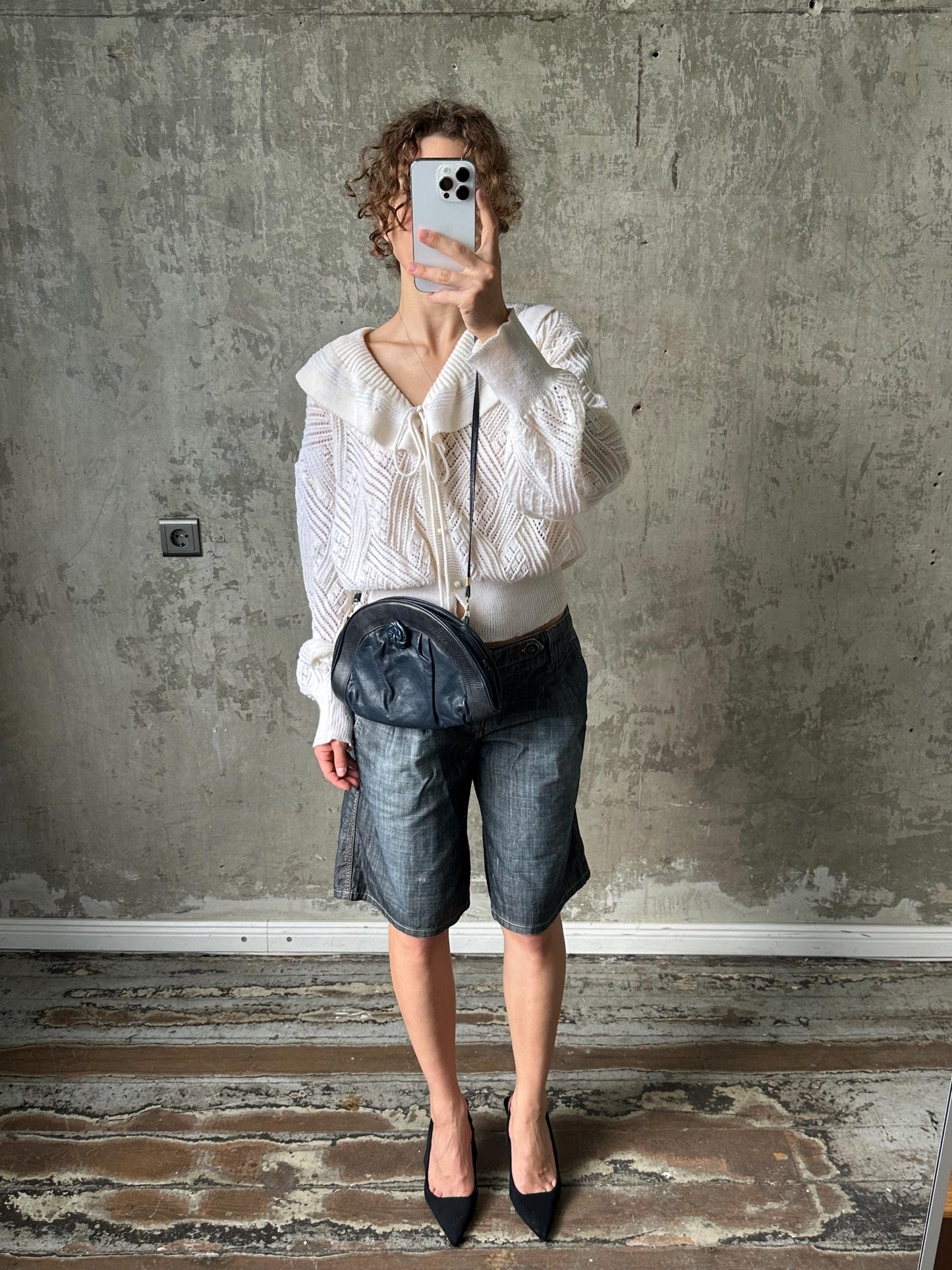 A person is taking a selfie with a white phone, standing in front of a concrete wall.
