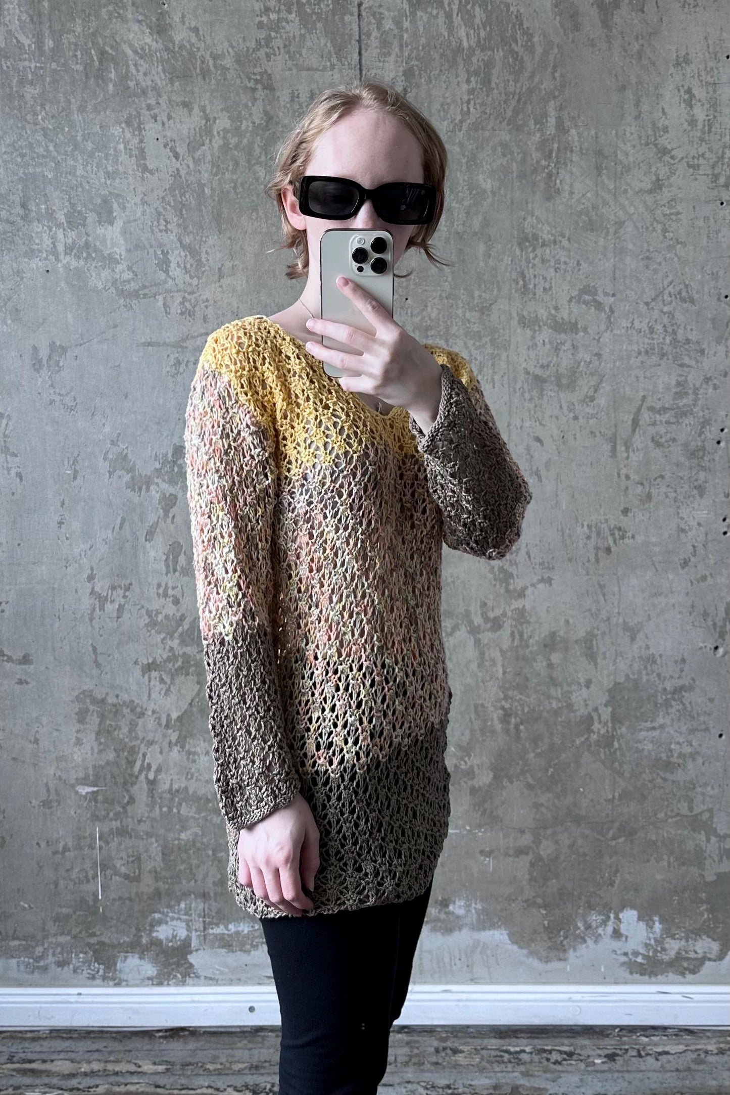 A person is taking a selfie with a smartphone, wearing a colorful, patterned sweater and sunglasses.