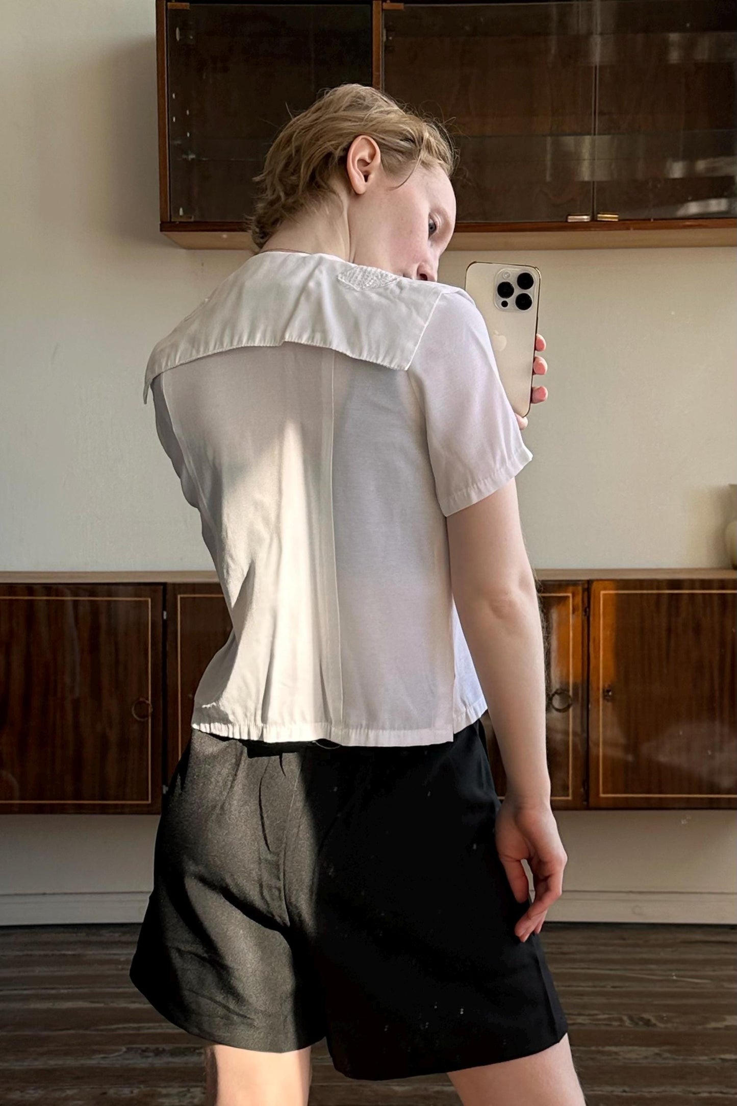 A person is taking a selfie with a white phone in front of a wooden cabinet.