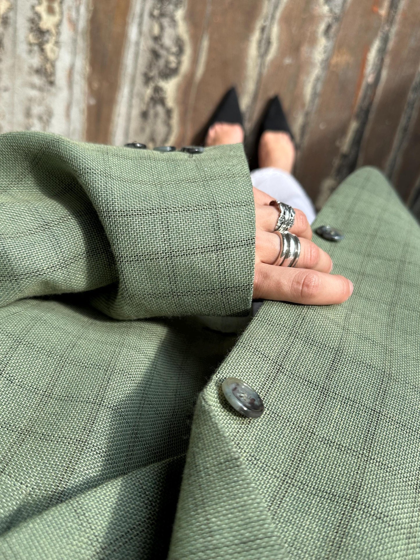 A close-up view of a person's hand wearing multiple rings, with a green plaid jacket partially visible.