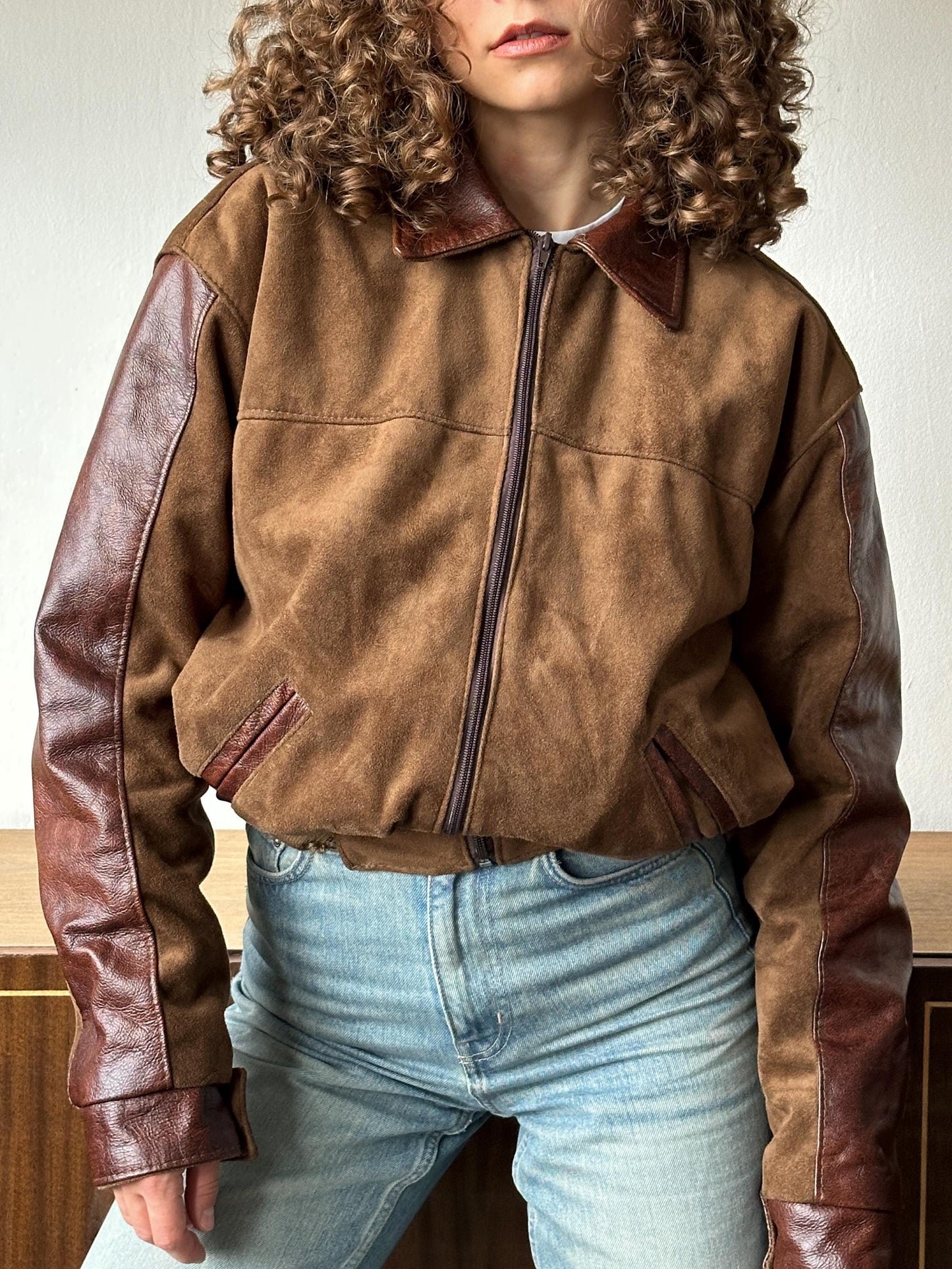 A person wearing a brown leather jacket and blue jeans is shown in the image.
