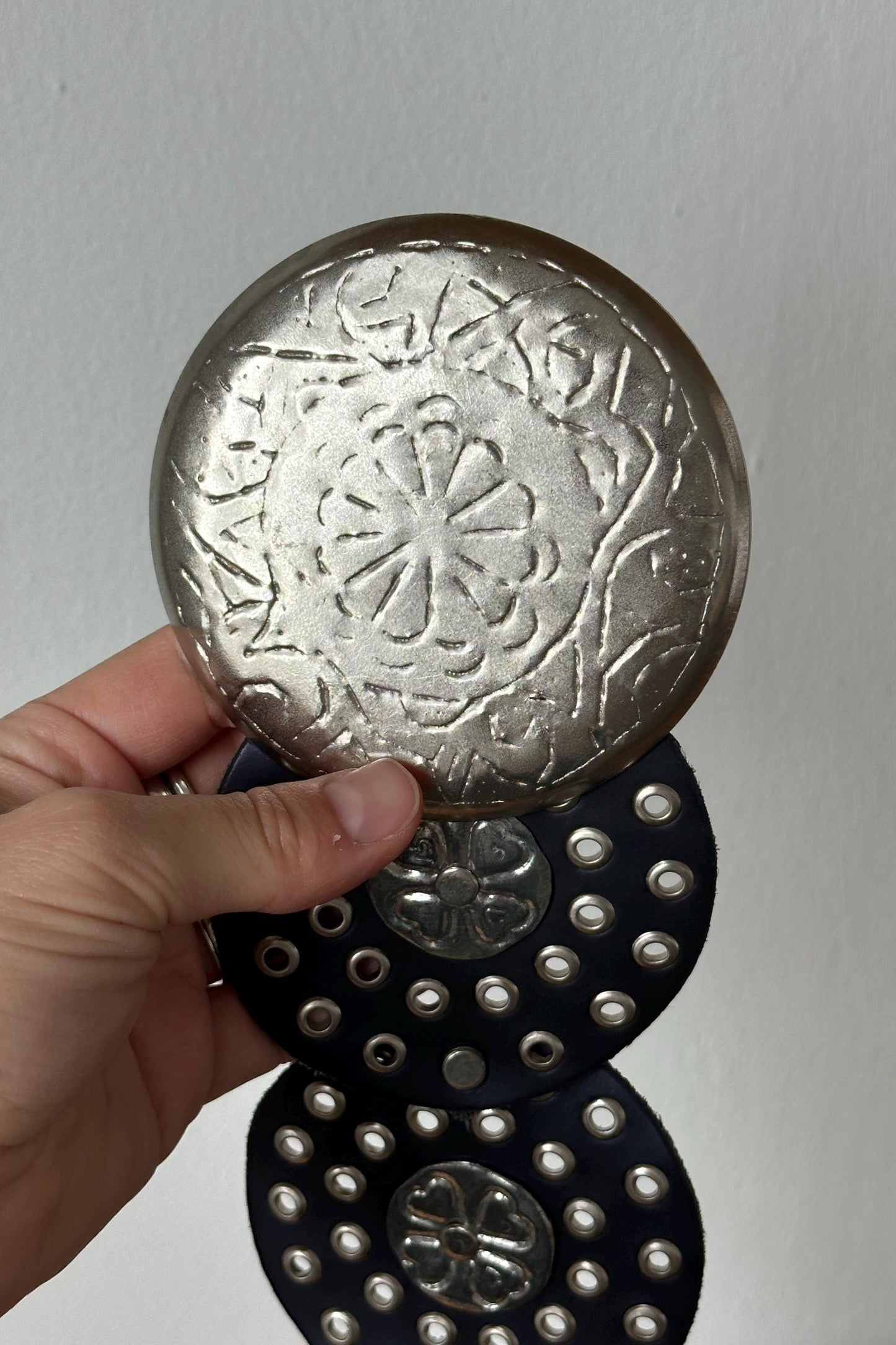 A hand is holding a circular metal object with a floral design, which appears to be a decorative piece.
