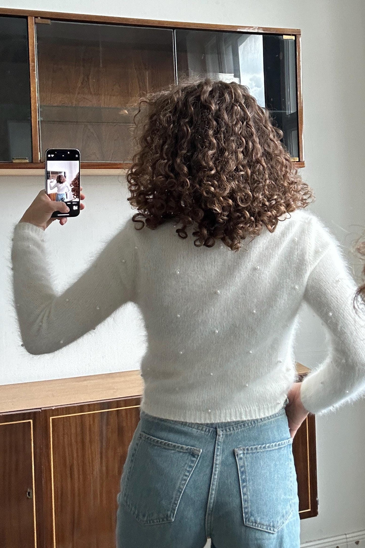 A person with curly hair is taking a selfie with a smartphone, holding the device up to their face.