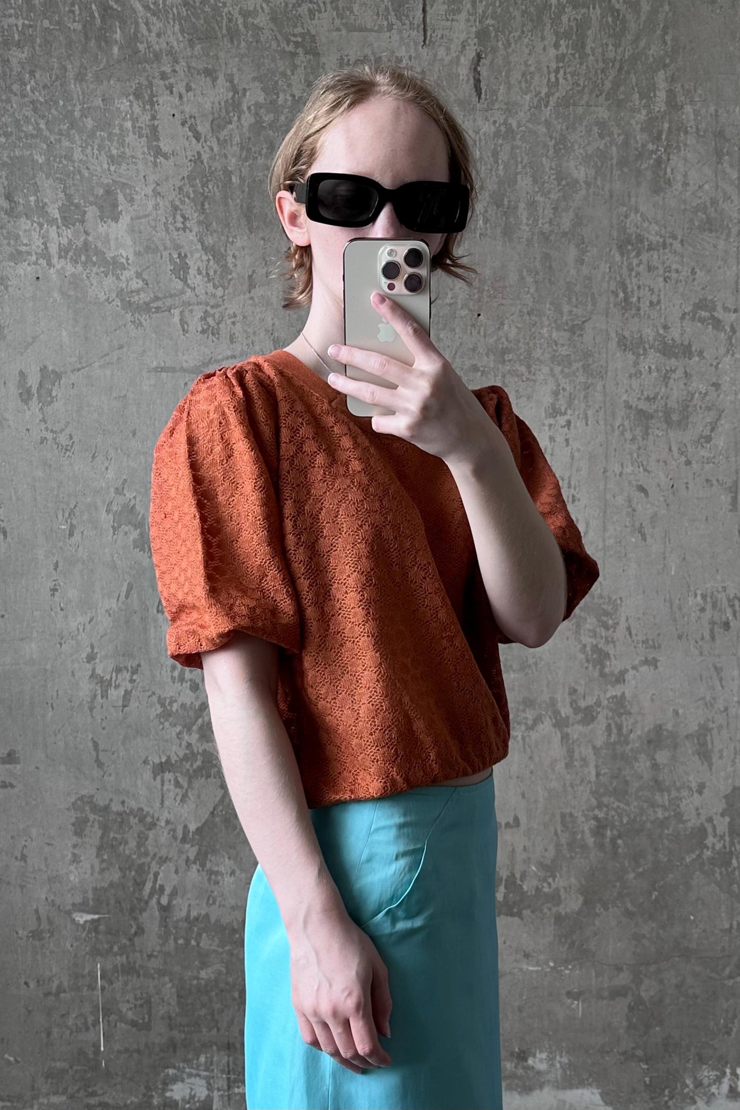 A person is taking a selfie with a smartphone, wearing a red puffed-sleeve top and a light blue skirt.