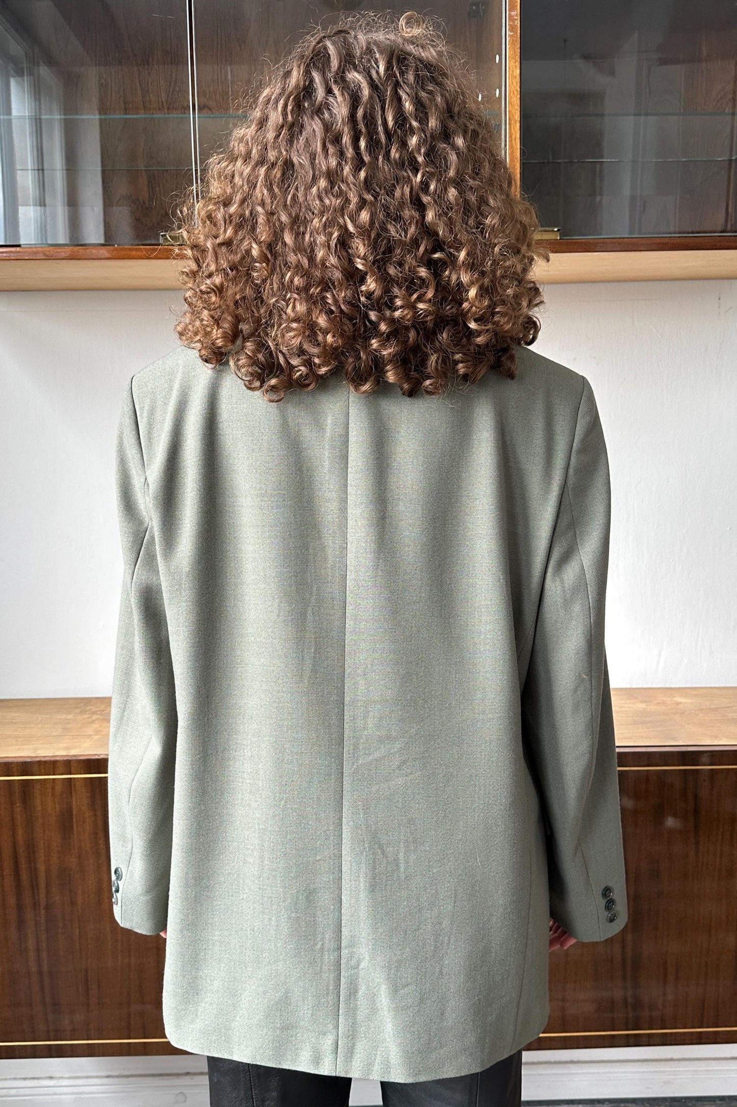 the back of a person with curly hair wearing a light green blazer.