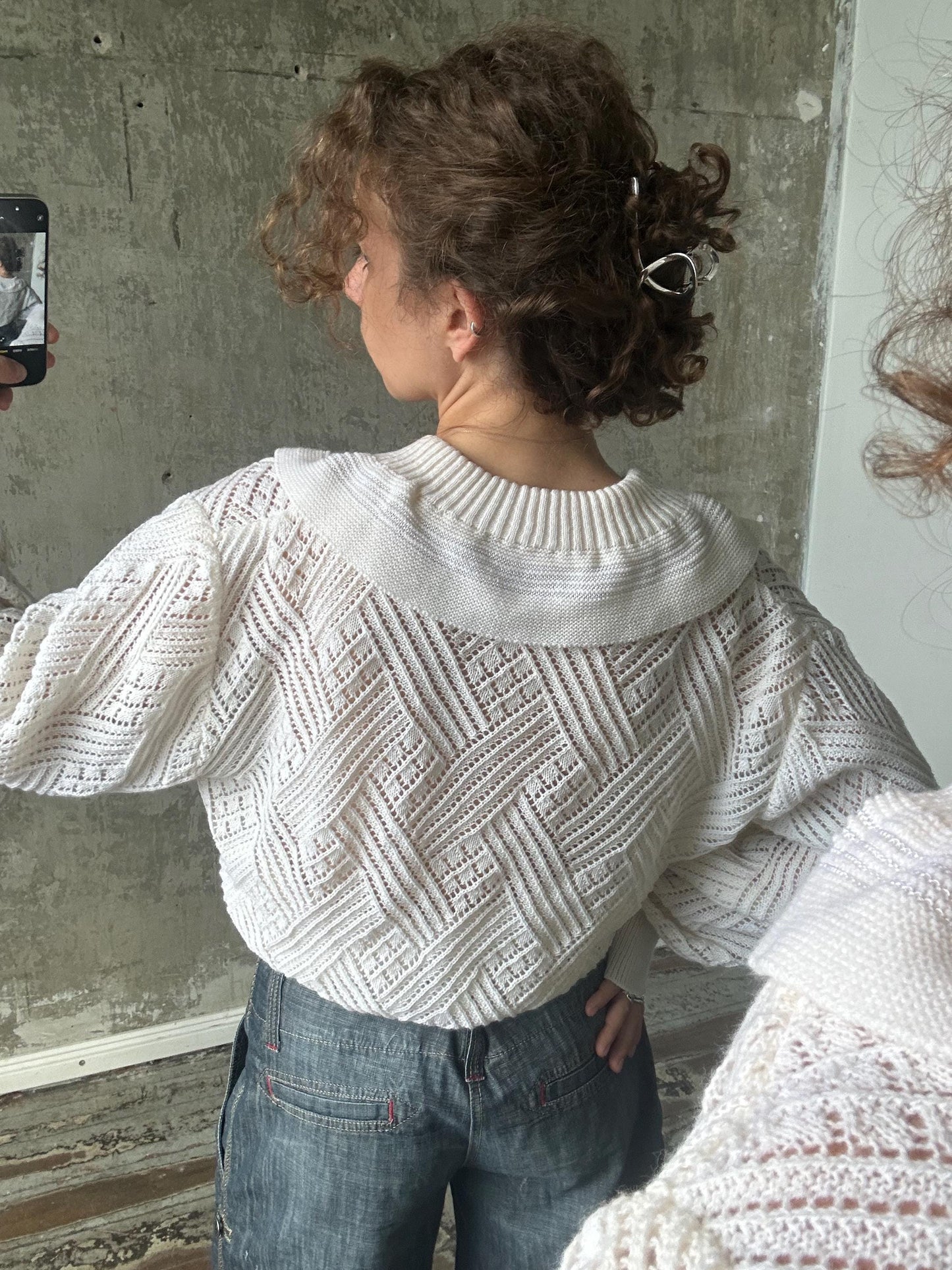 a person taking a selfie with a white sweater and jeans, capturing their back view.