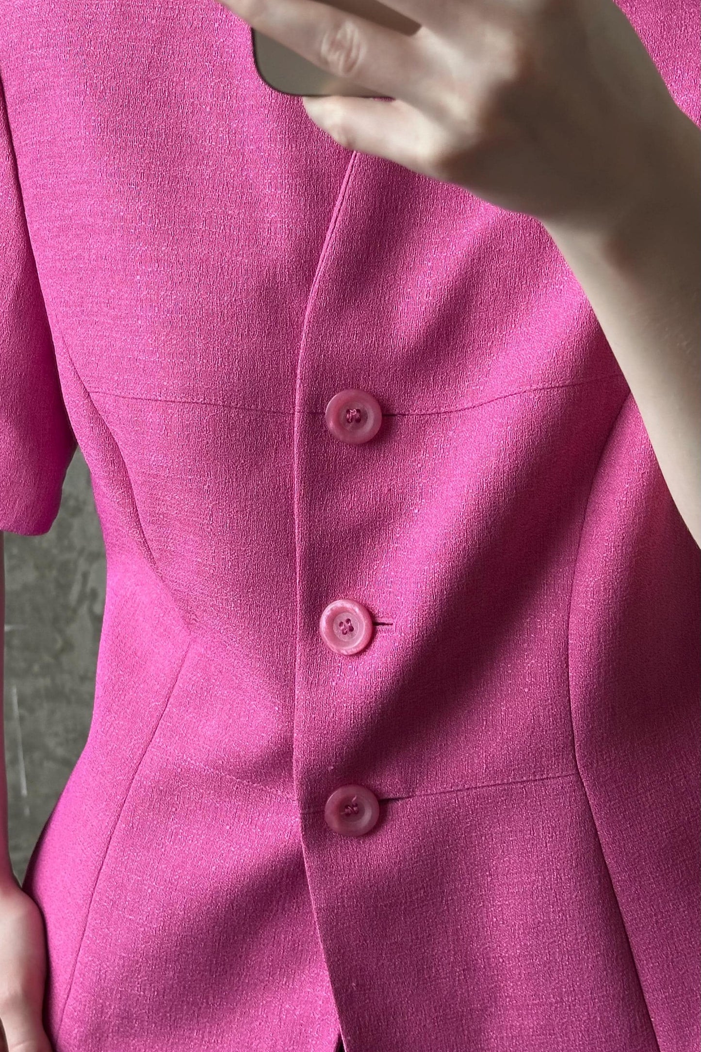 A close-up view of a person wearing a bright pink blazer with three buttons.