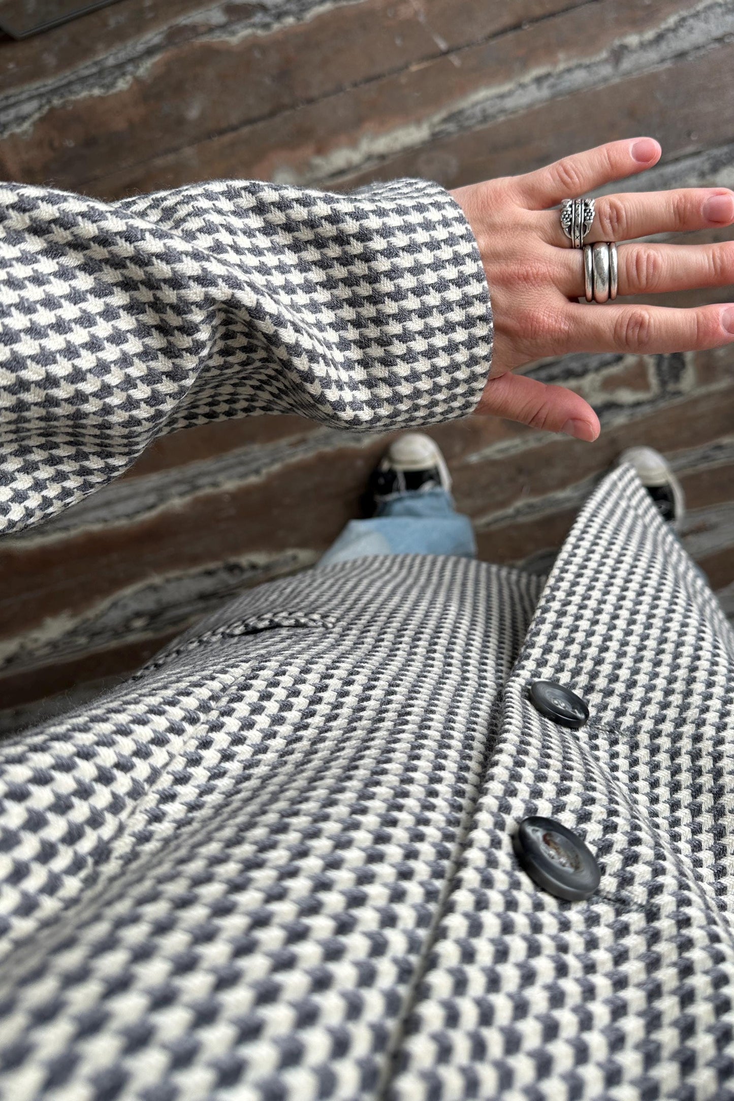 A close-up view of a person's hand wearing a black and white checkered jacket, with a ring visible on one of the fingers.