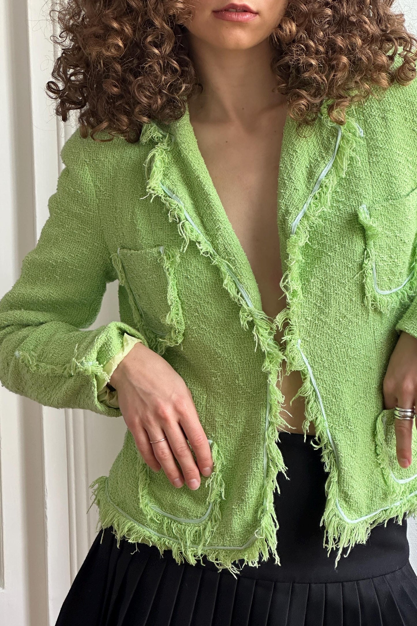 A close-up of a woman wearing a lime green tweed jacket with fringed edges and a black skirt.
