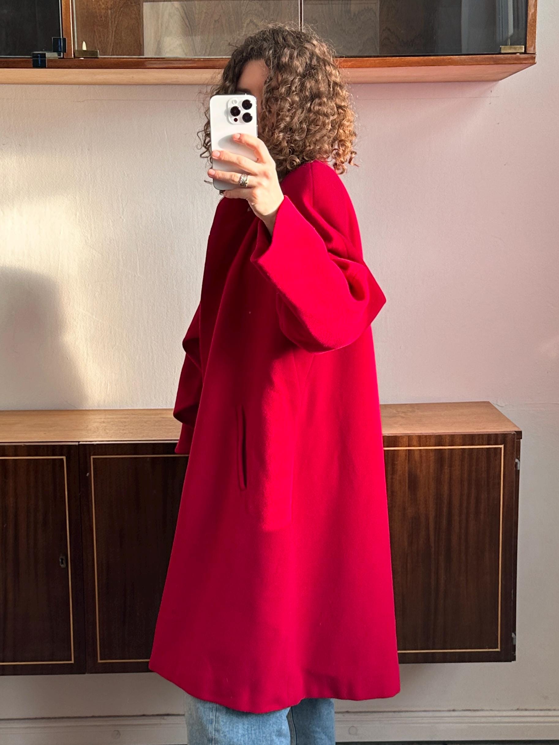 A person is taking a selfie with a white phone, wearing a red coat.