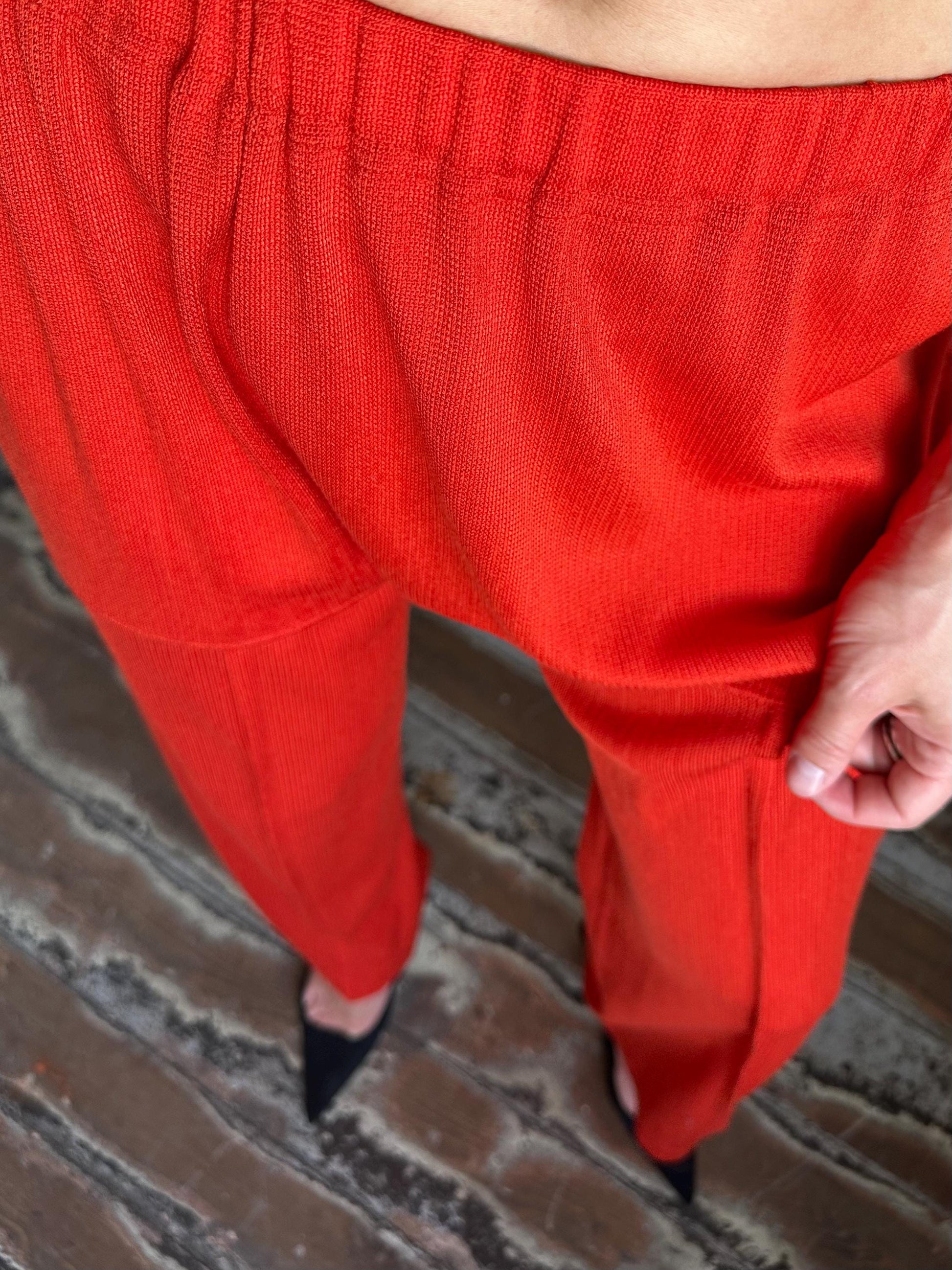 A close-up view of a person wearing bright red pants, standing on a wooden floor.