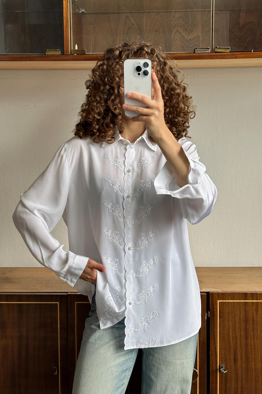 A person with curly hair is taking a selfie with a white iPhone, holding the device up to their face.