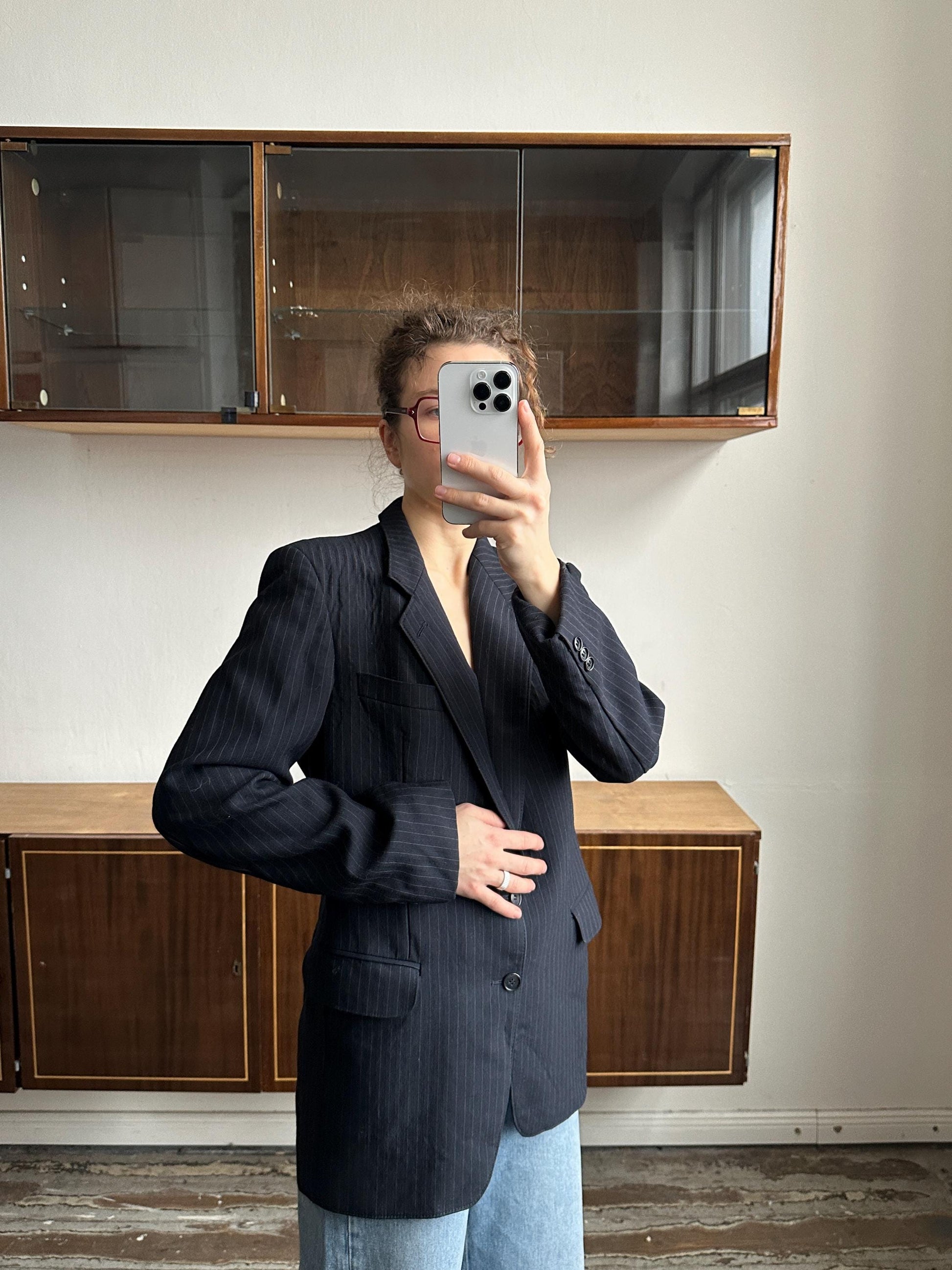 A person is taking a selfie in front of a wooden cabinet, holding a smartphone in their hand.
