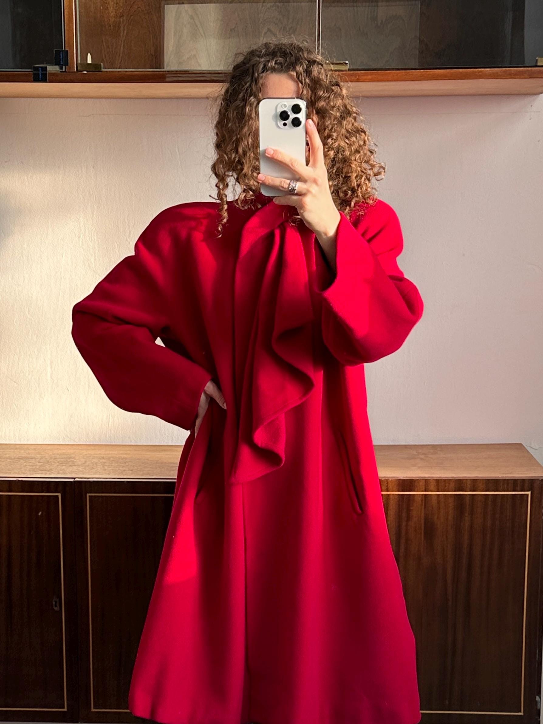 A person wearing a red coat is taking a selfie with a white phone.