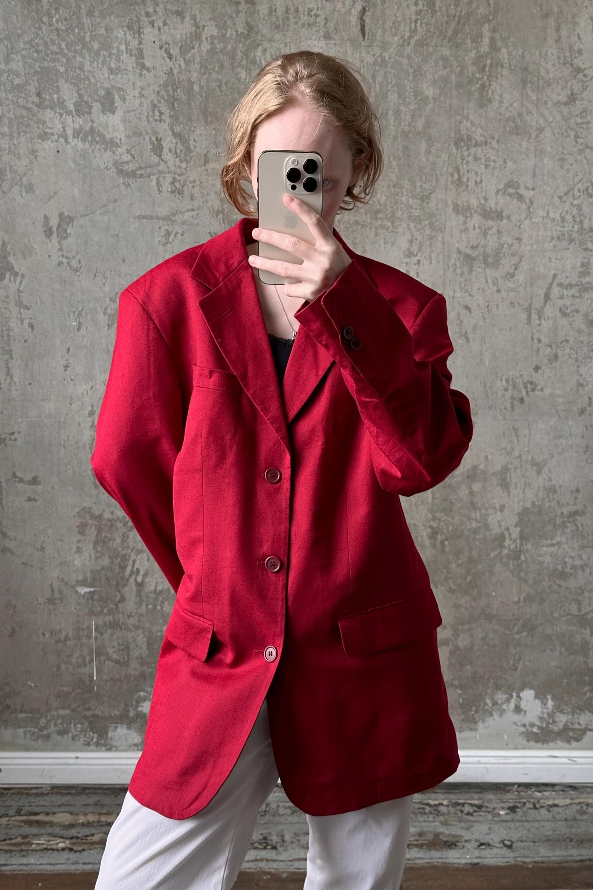 A person wearing a red blazer is taking a selfie with a smartphone.