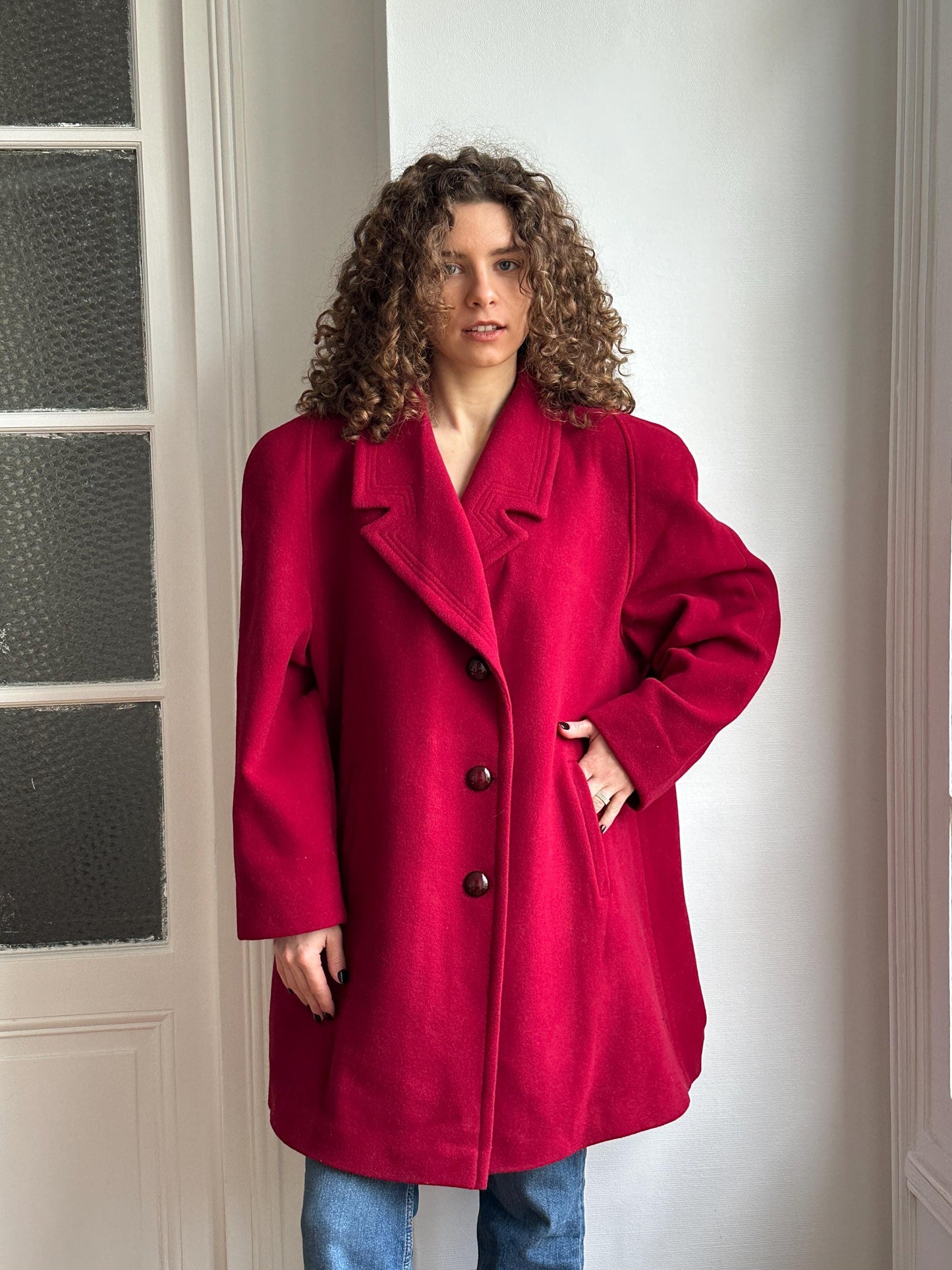 A person wearing a red coat is standing in front of a window.