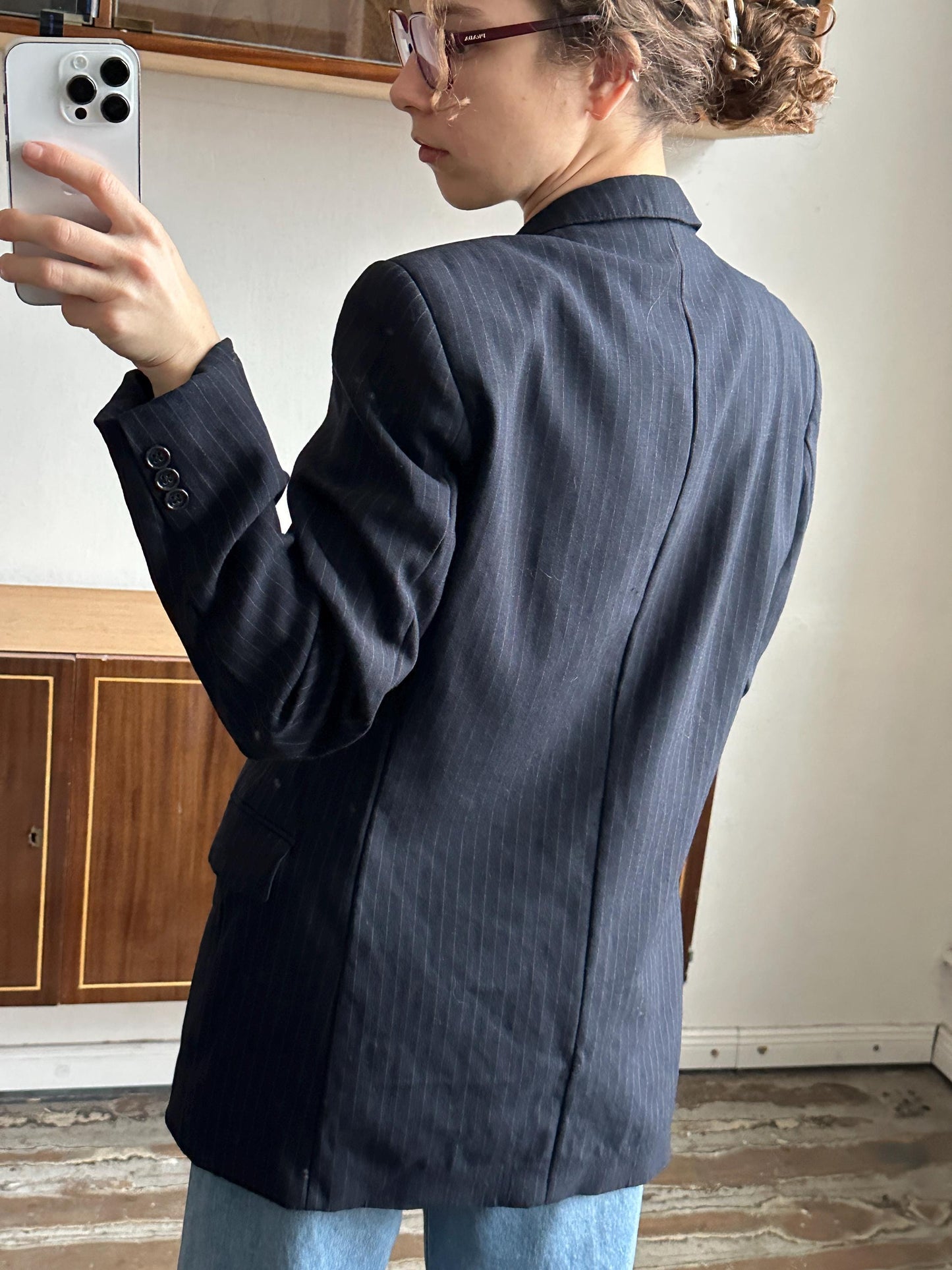 A person wearing a dark suit jacket is leaning over a wooden cabinet, with a smartphone visible in the background.