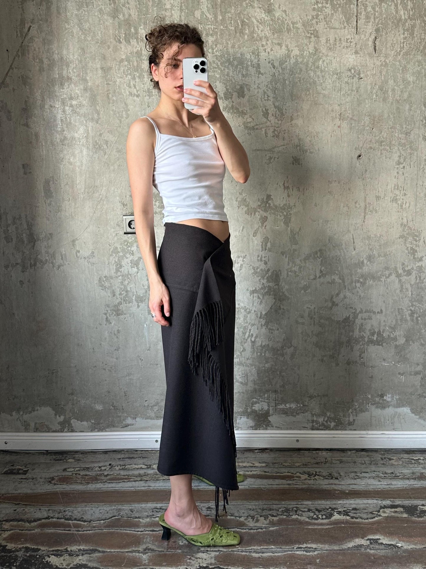 A woman is taking a selfie with her phone, standing in front of a concrete wall.