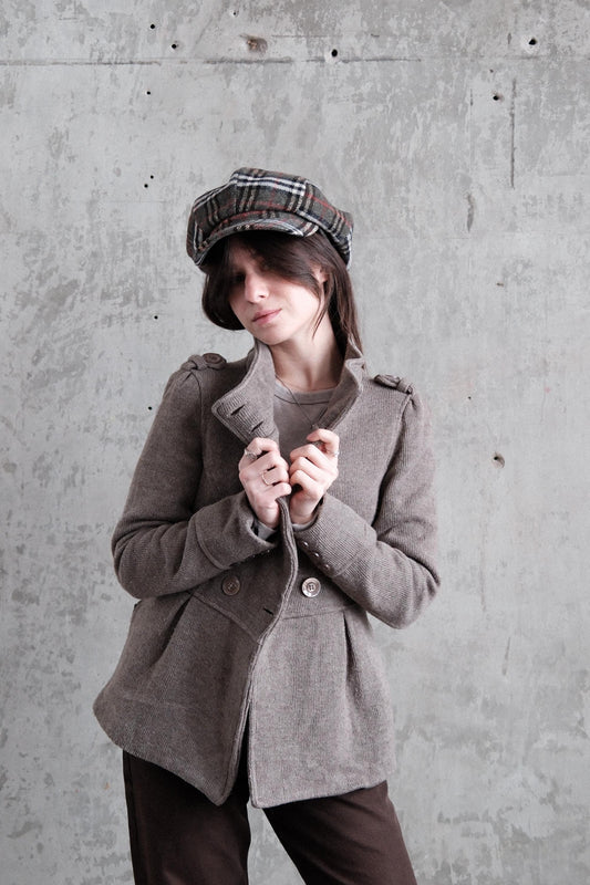 A person wearing a gray coat and a plaid hat is lying on a concrete floor, looking down.