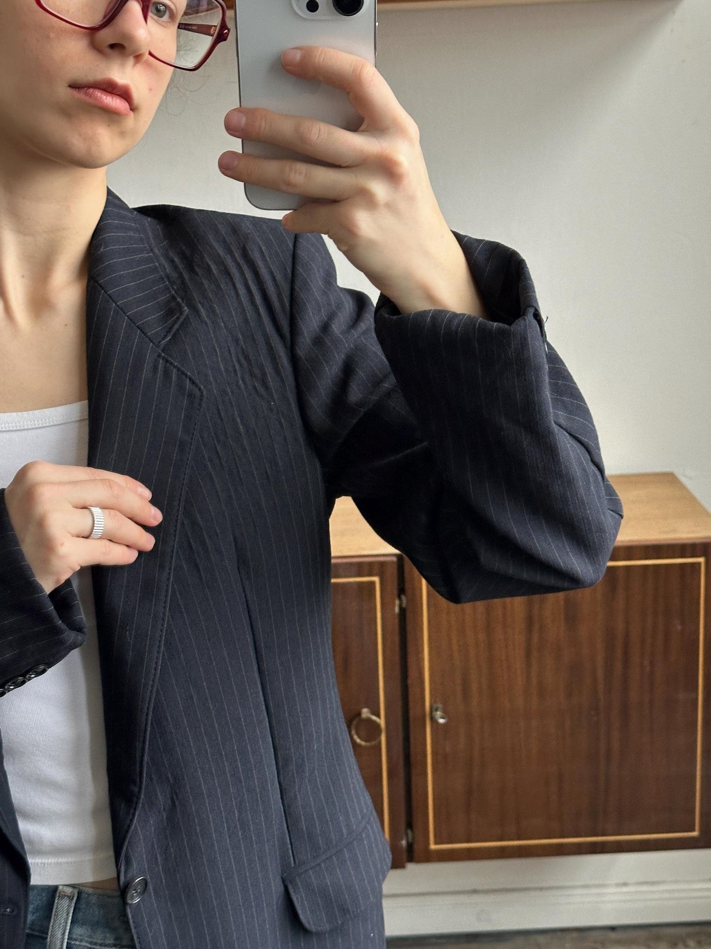A person wearing a black suit and glasses is taking a selfie with a smartphone.