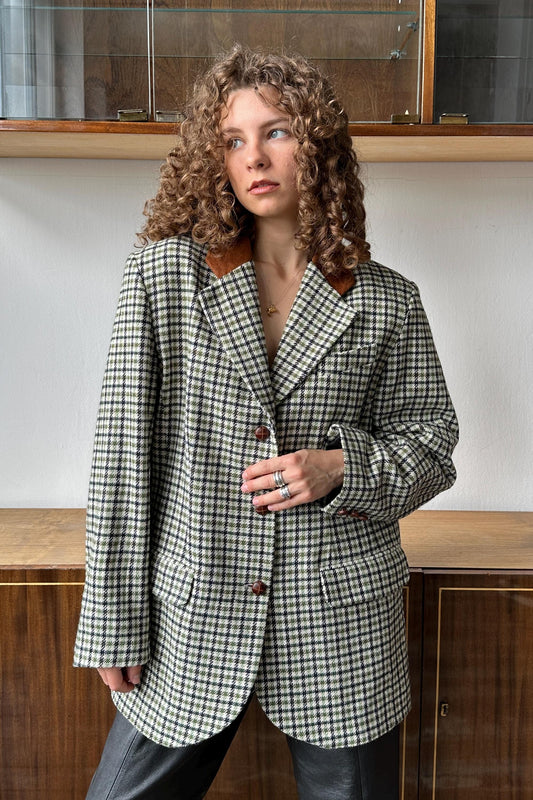 A woman with curly hair wearing a black and white checkered jacket stands in front of a wooden cabinet.