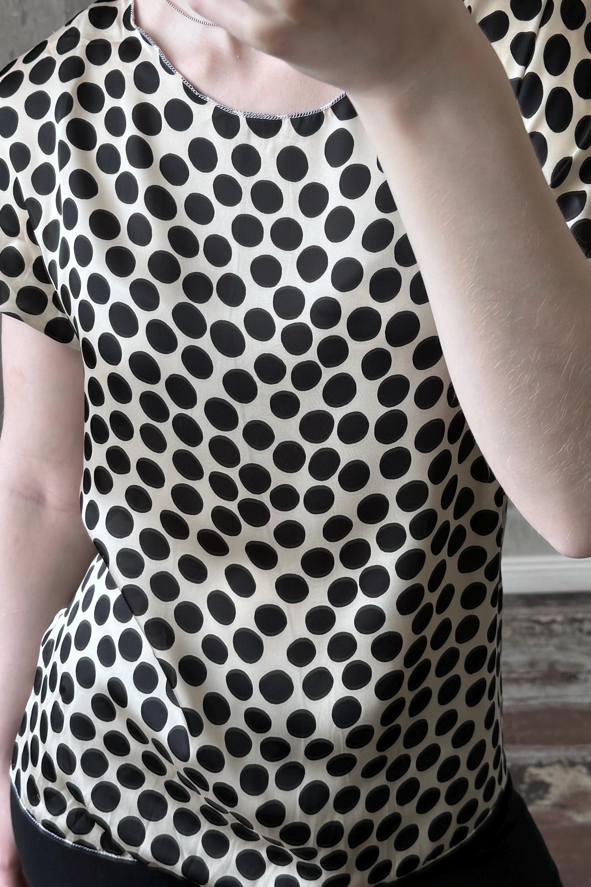 a person wearing a black and white polka dot blouse, with their hand covering their face.