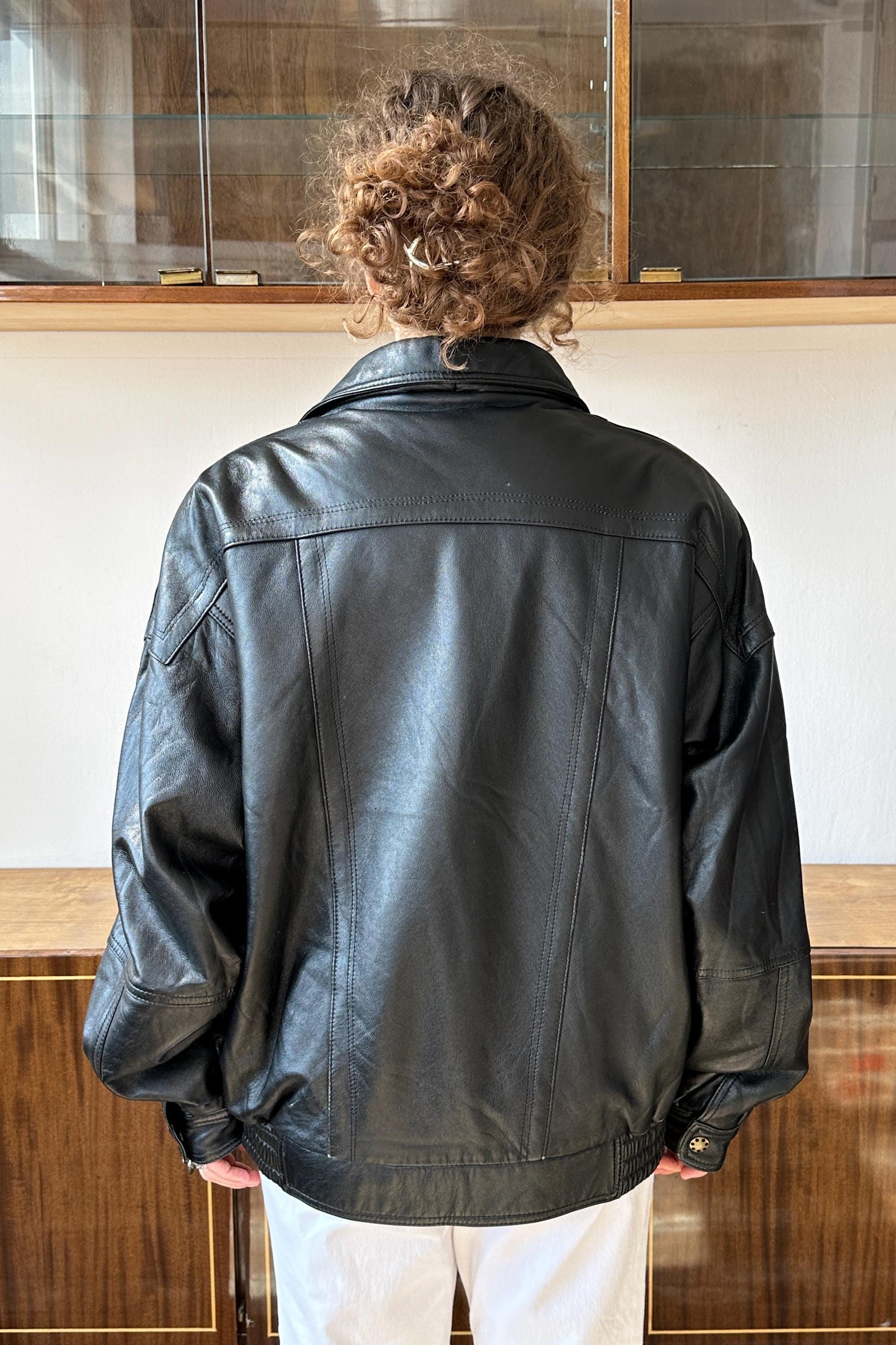 A person wearing a black leather jacket stands in front of a glass display case.